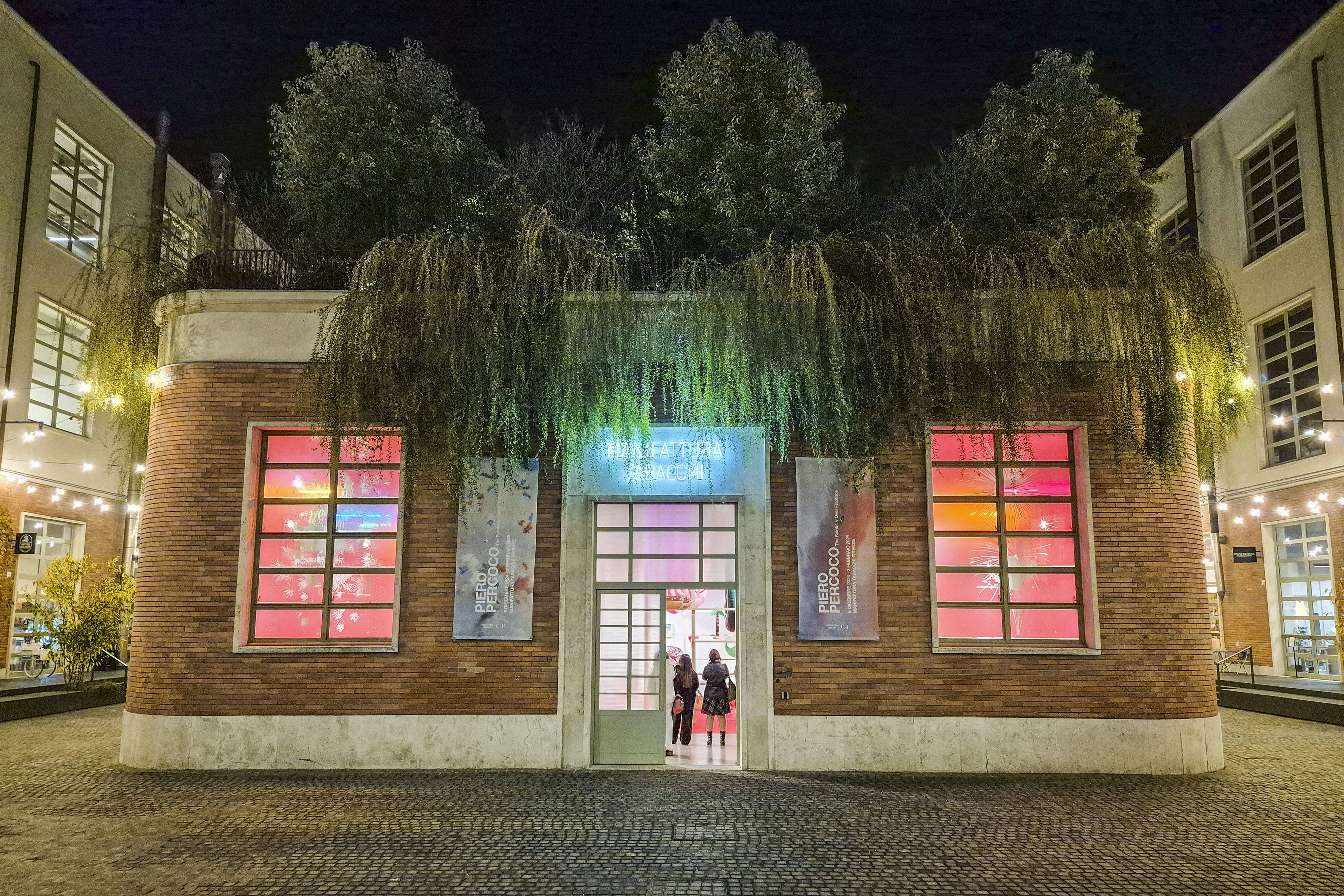 A renovated former industrial building contains displays of contemporary art featuring neon lights. Trees and bushes grow on the roof of the building.