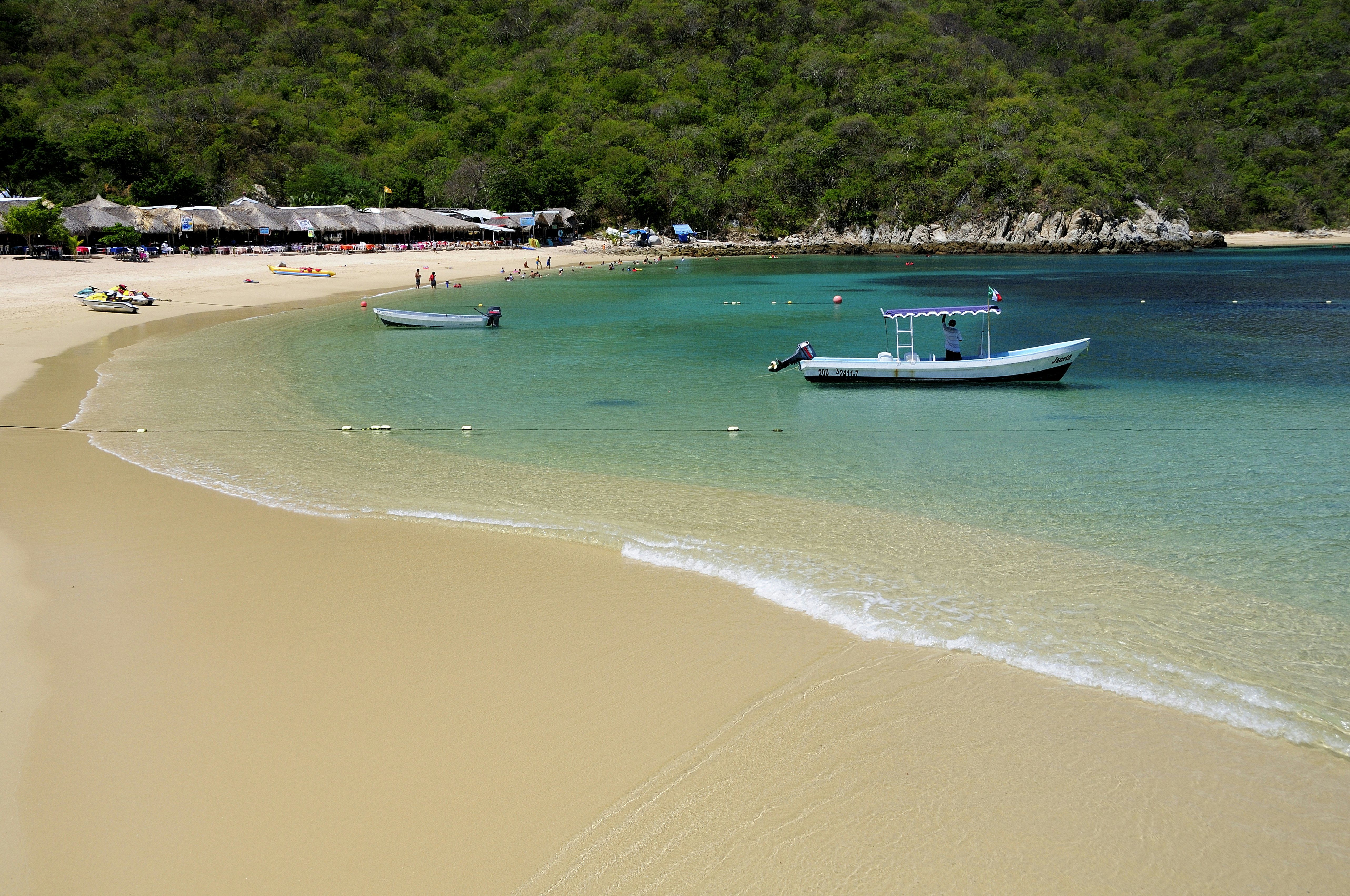 Two boats in shallow turquoise water by a sandy beach in Mexico.