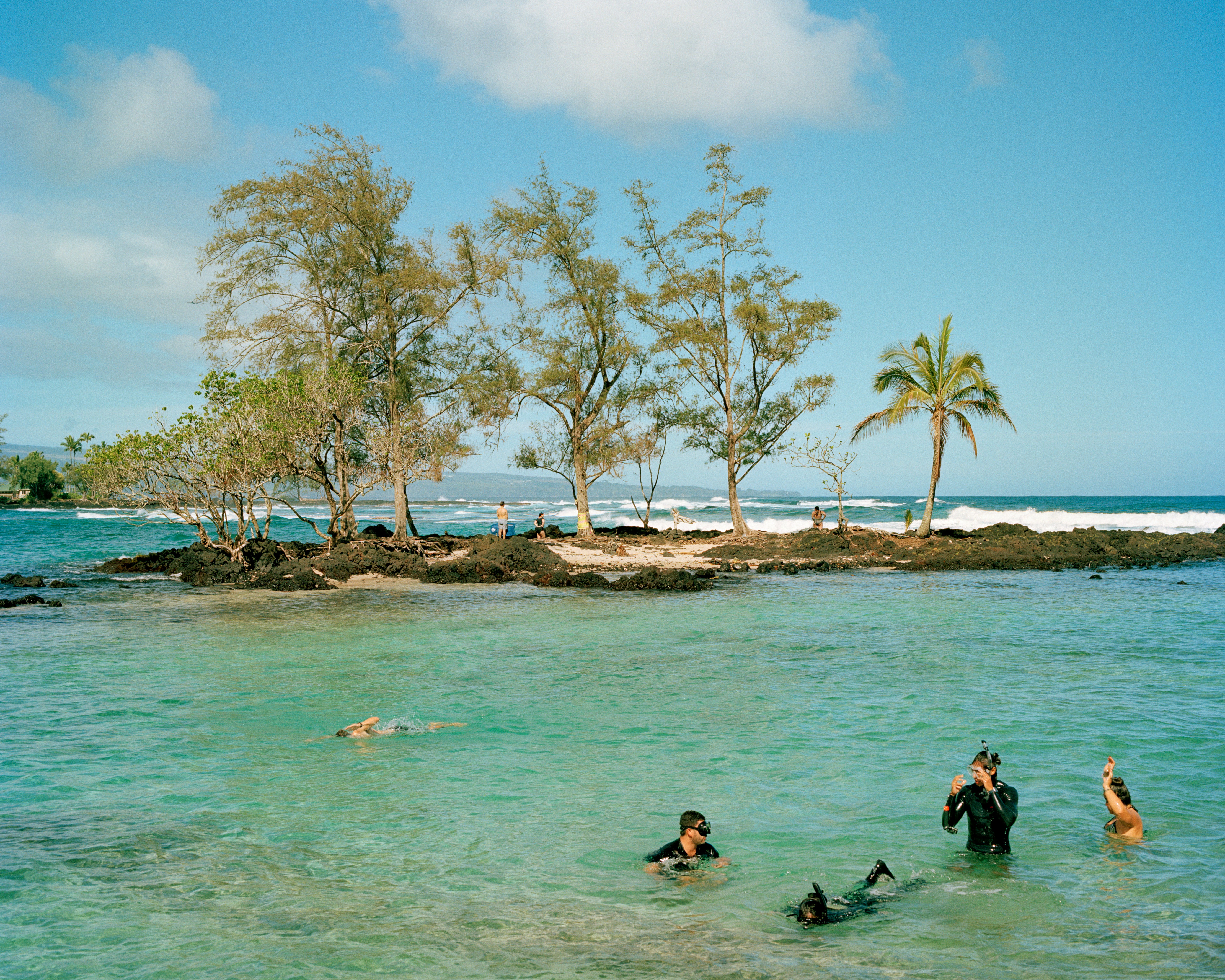 Snorkelers in shallow water in front of a sand and rock reef in Hawai'i.