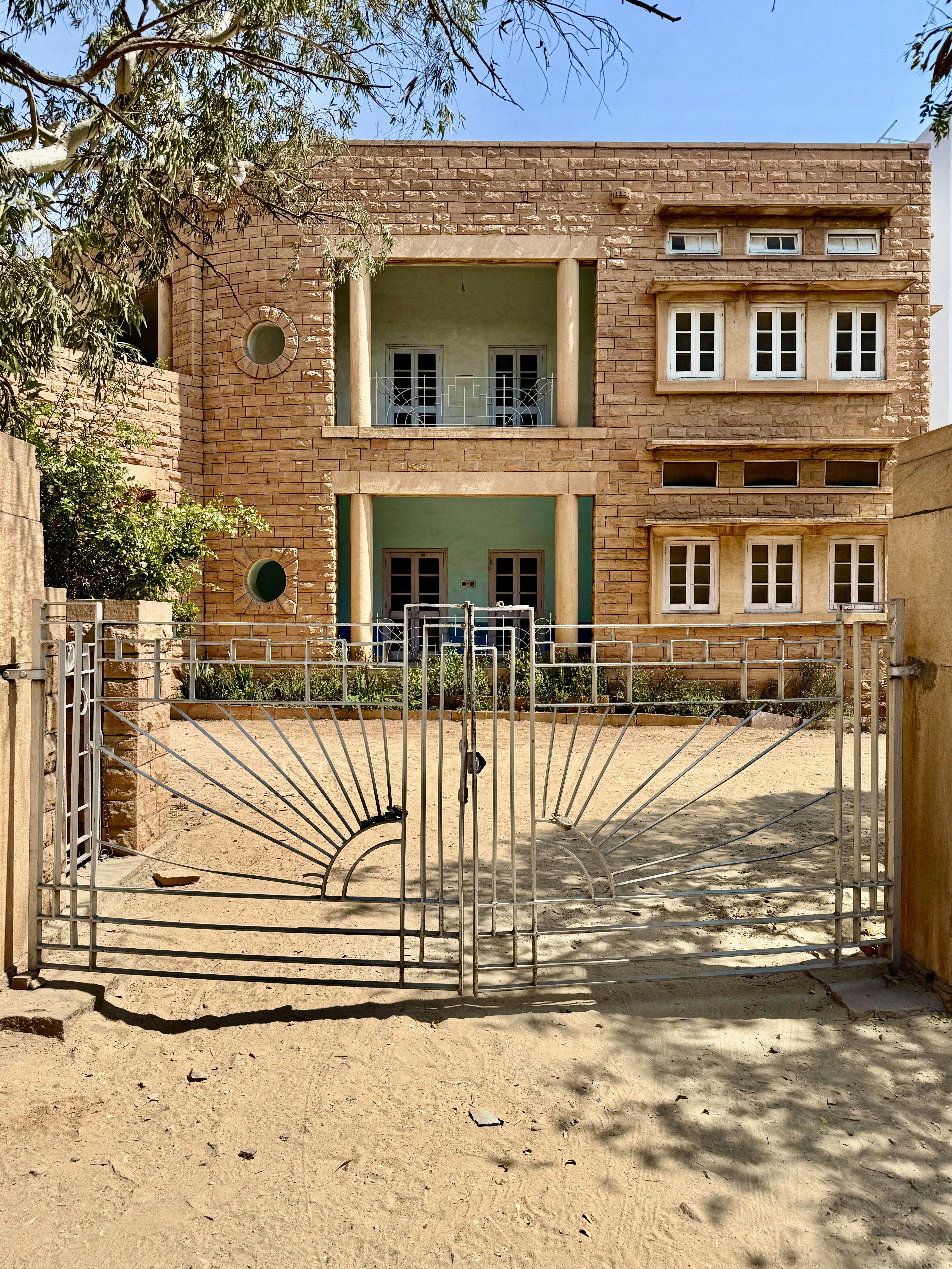 A tan stone building behind a gate has alcoves painted pale green.