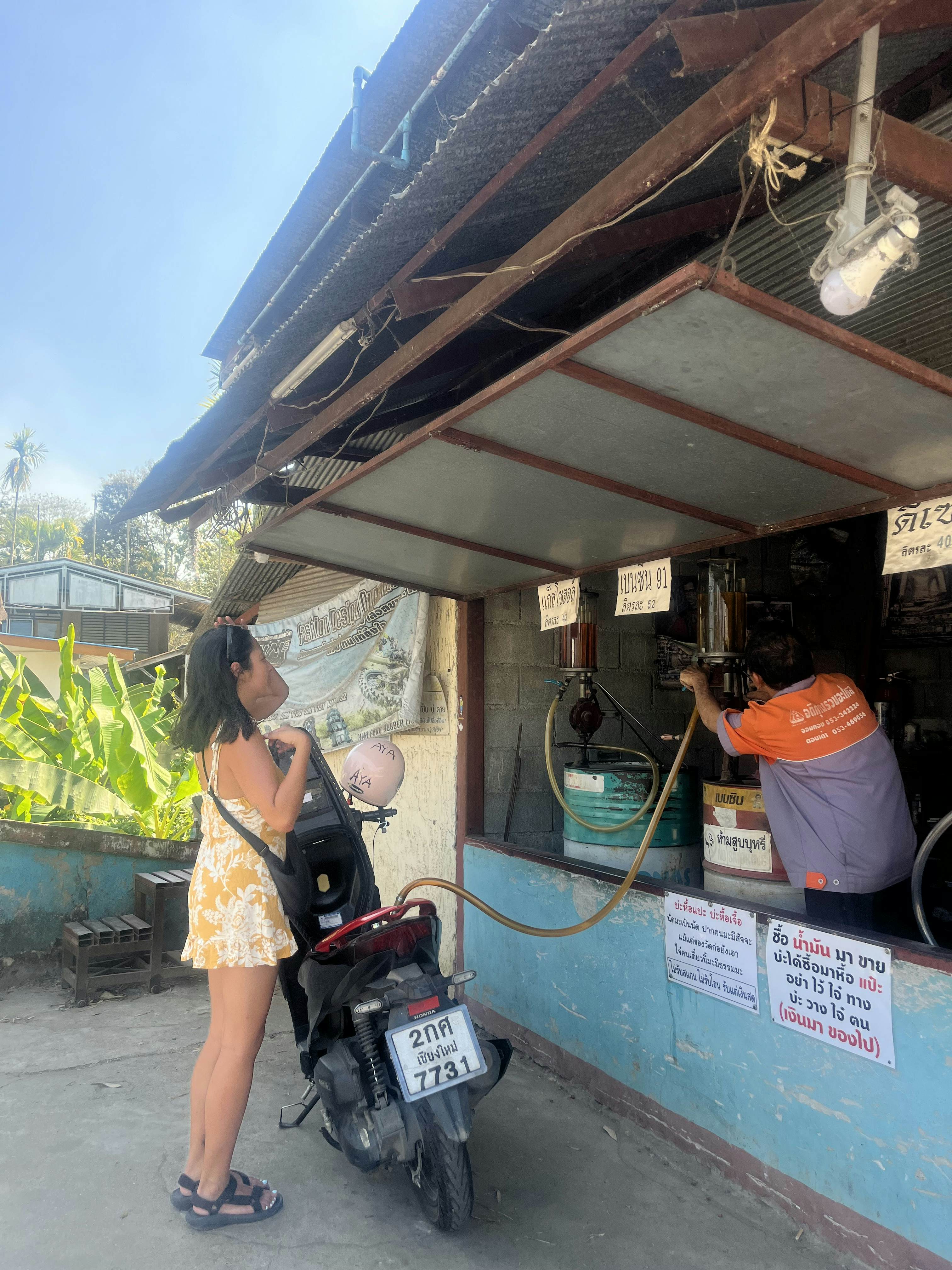 A woman stops at a kiosk selling fuel to refill the tank of her scooter.
