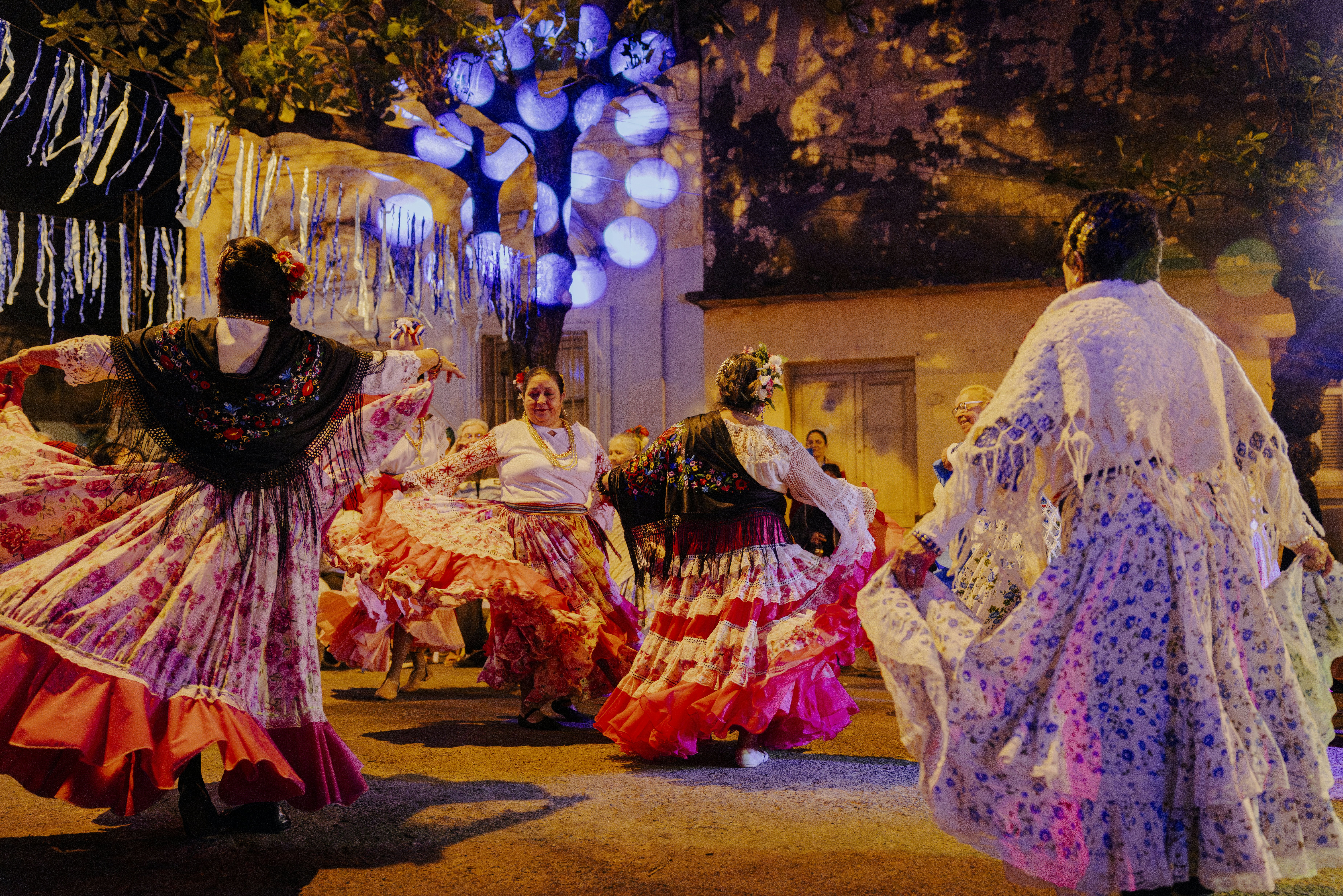 Female dancers in ruffled skirts and shawls perform on a city street after dark.