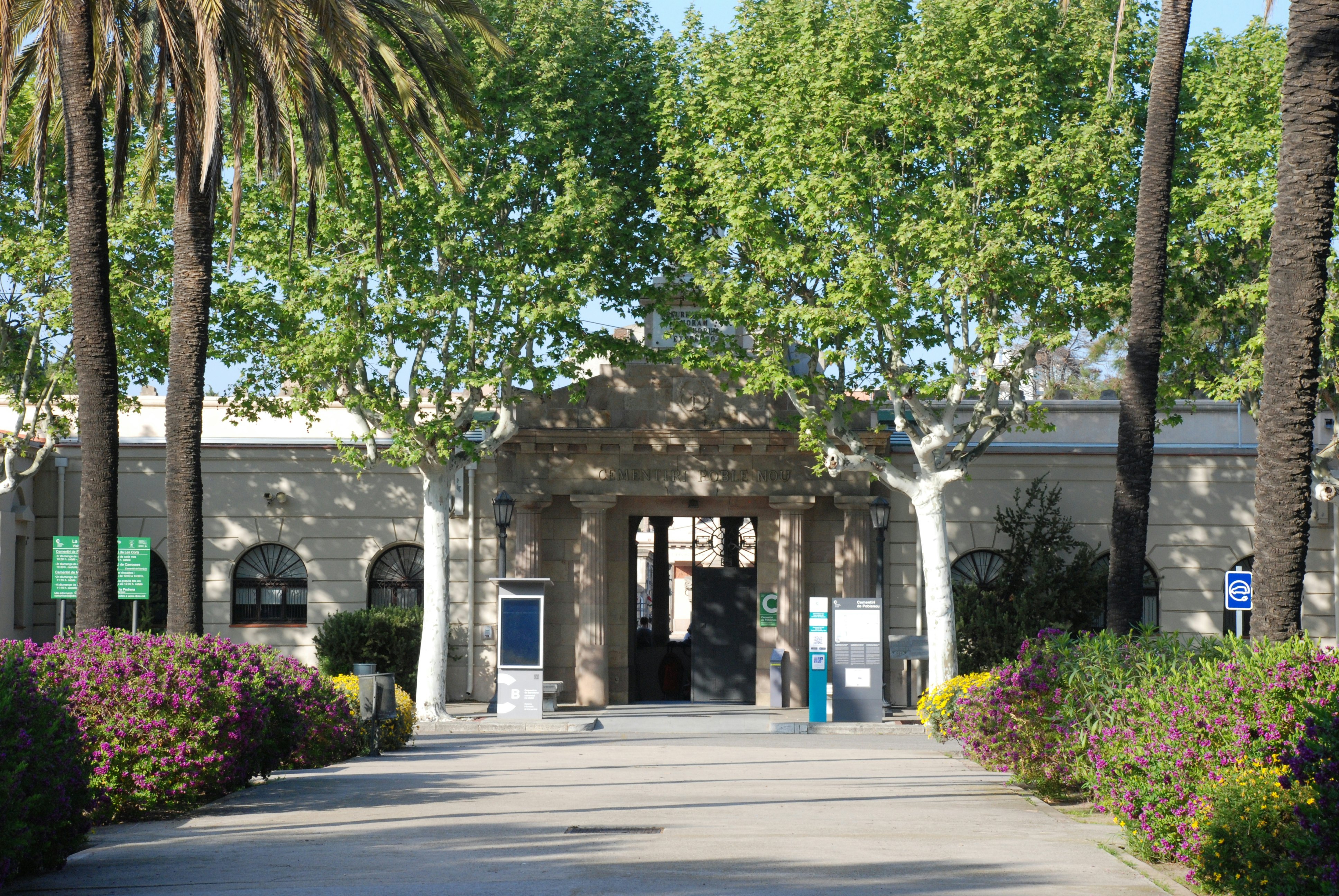 Entrance to Cemintiri del Poblenou with trees and floral bushes nearby.