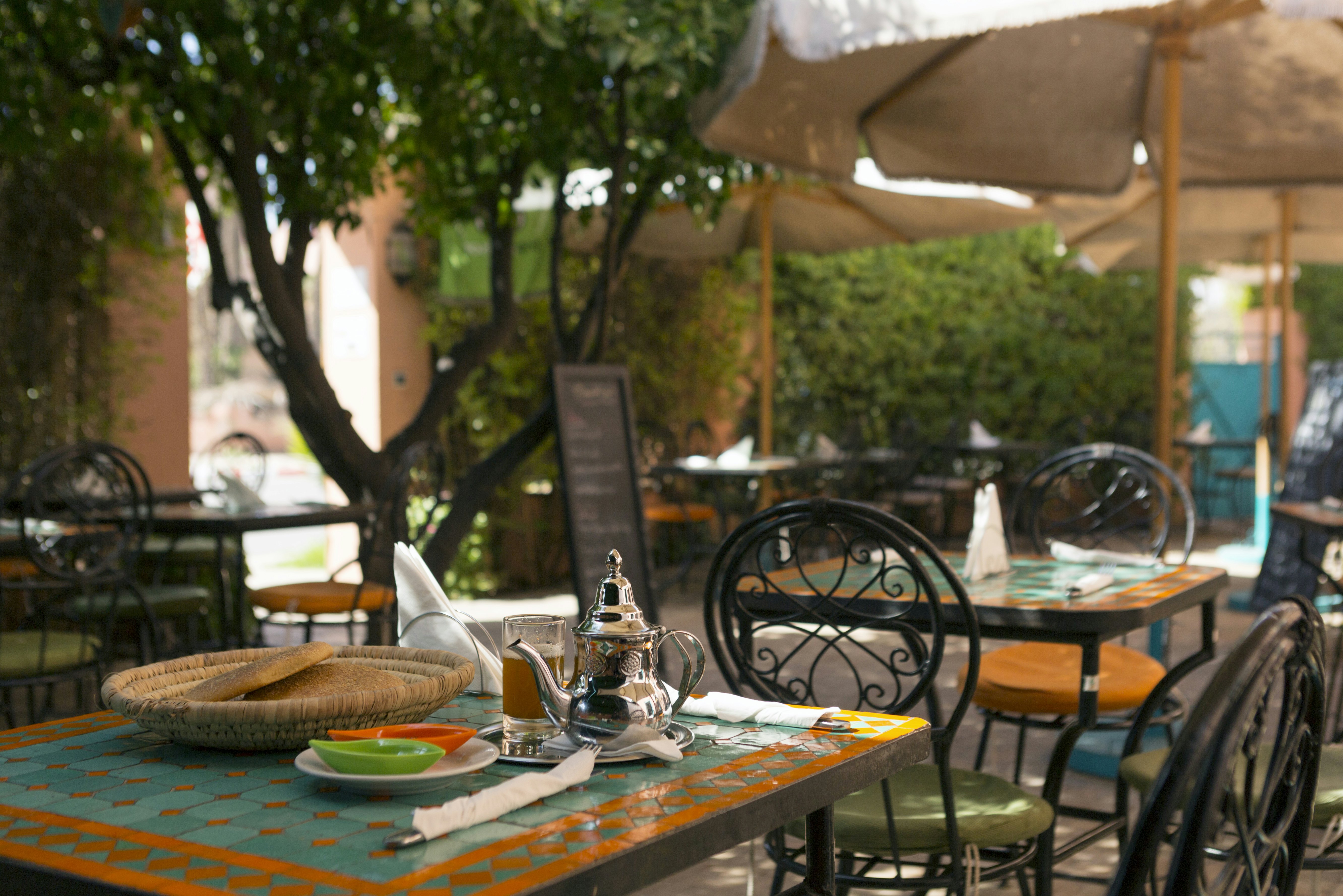 A table in a restaurant courtyard with a basket of flatbread and a silver pot next to a glass of tea.