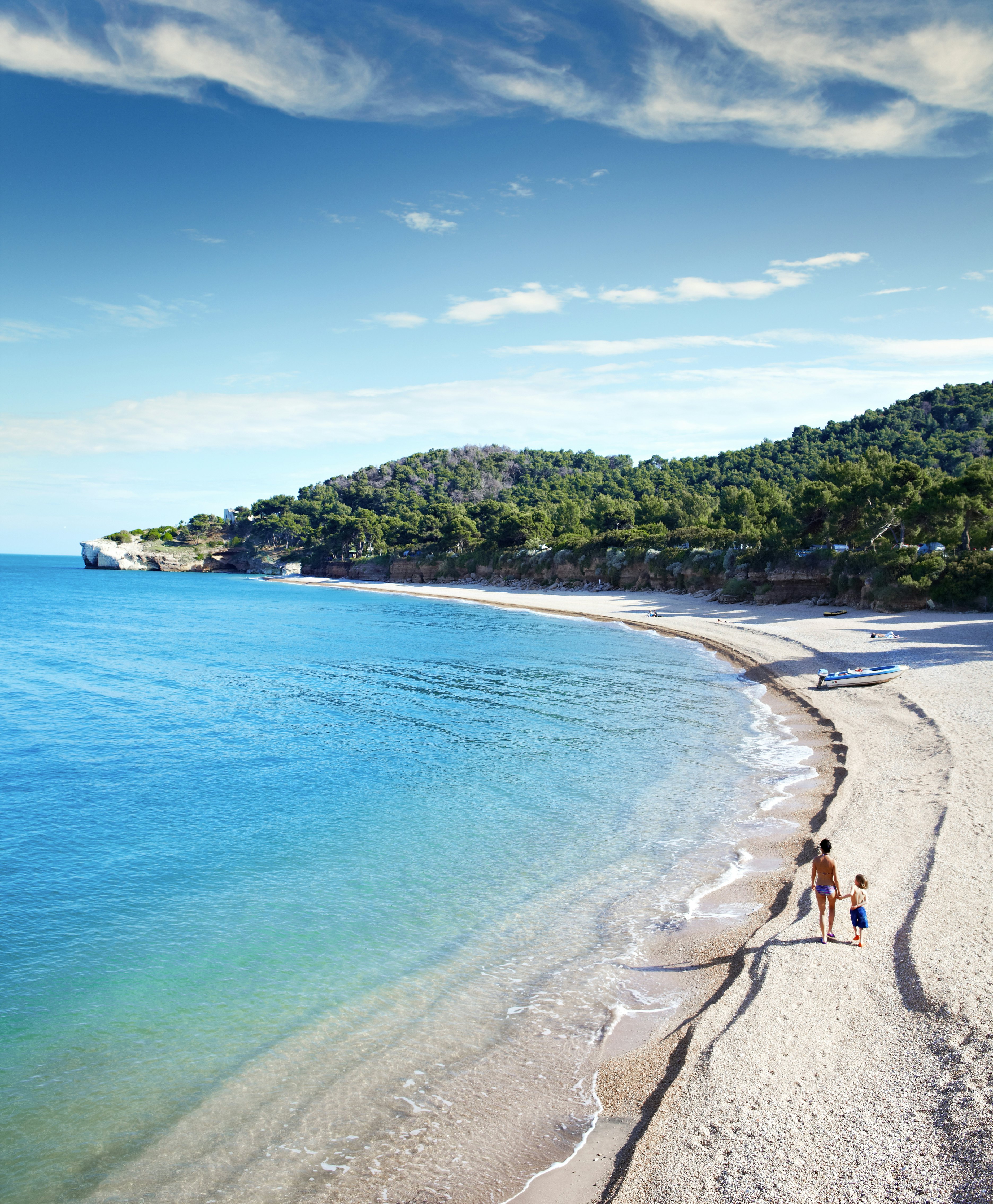 Woman and child walking on a beach with bright blue water