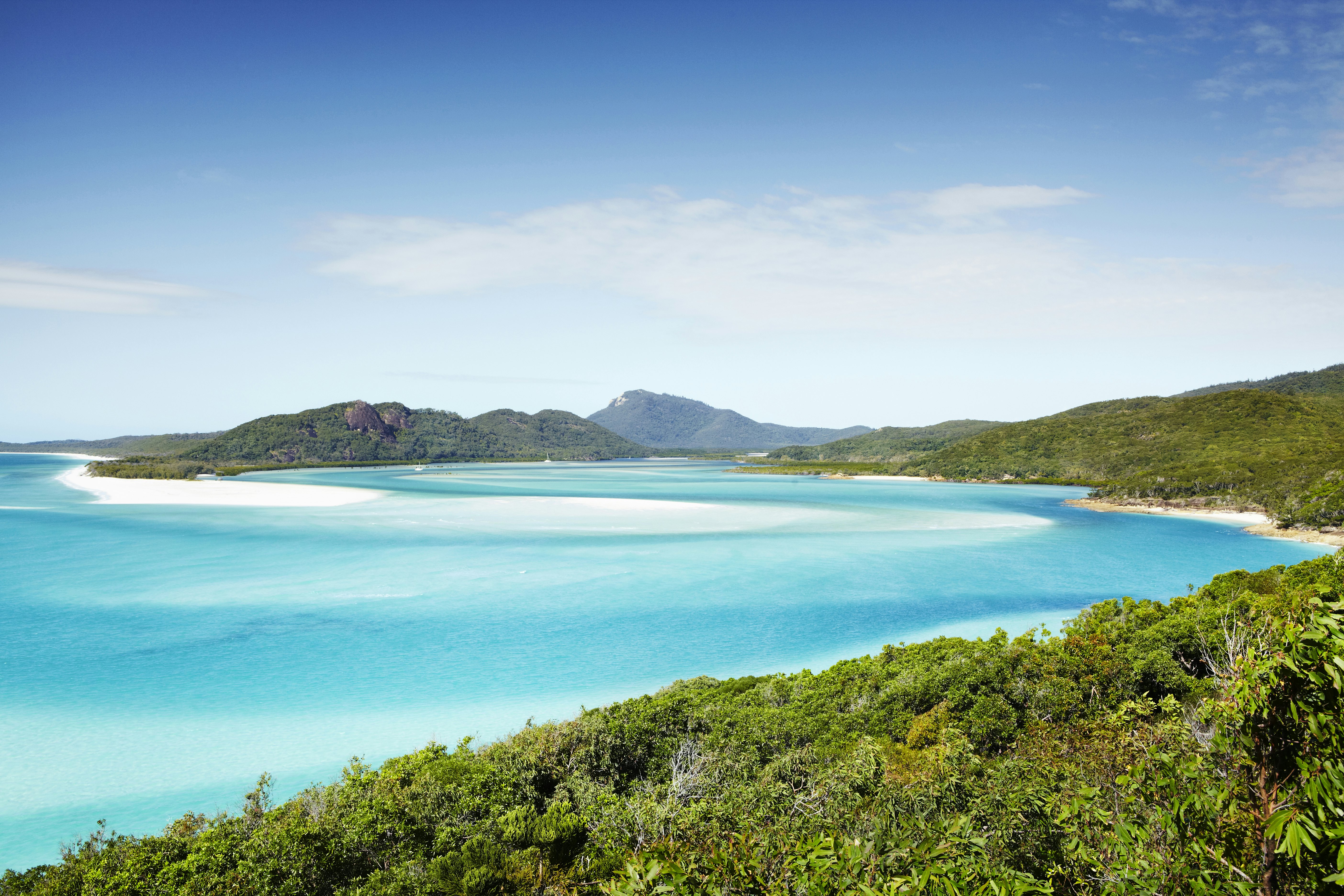 A vast bay near a tropical island with turquoise waters and bright white sands.