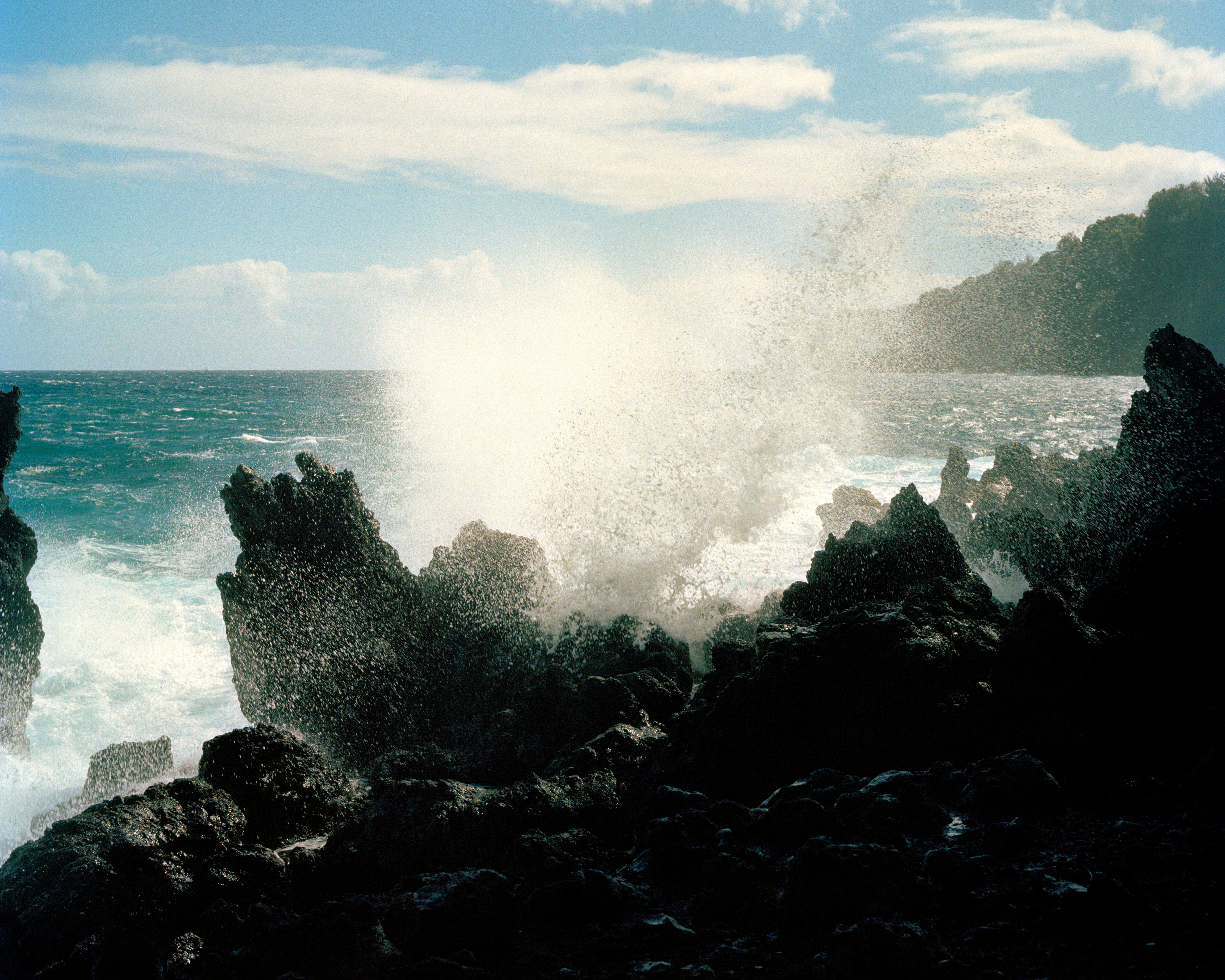 Waves break over a black rocky shoreline on Hawai'i.