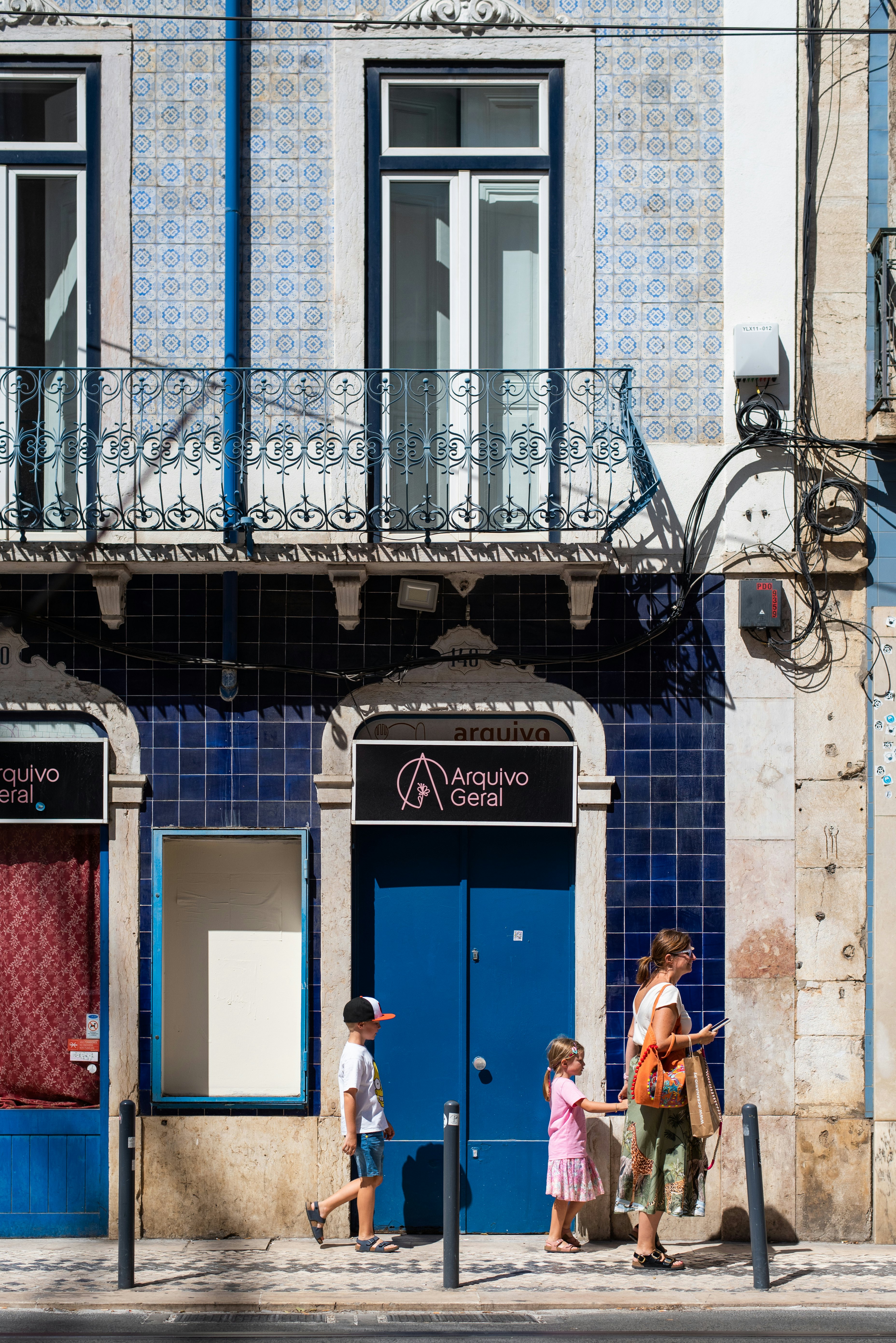 A family visiting Lisbon, Portugal passed doorways with tiled walls. The woman holds her childs hand.