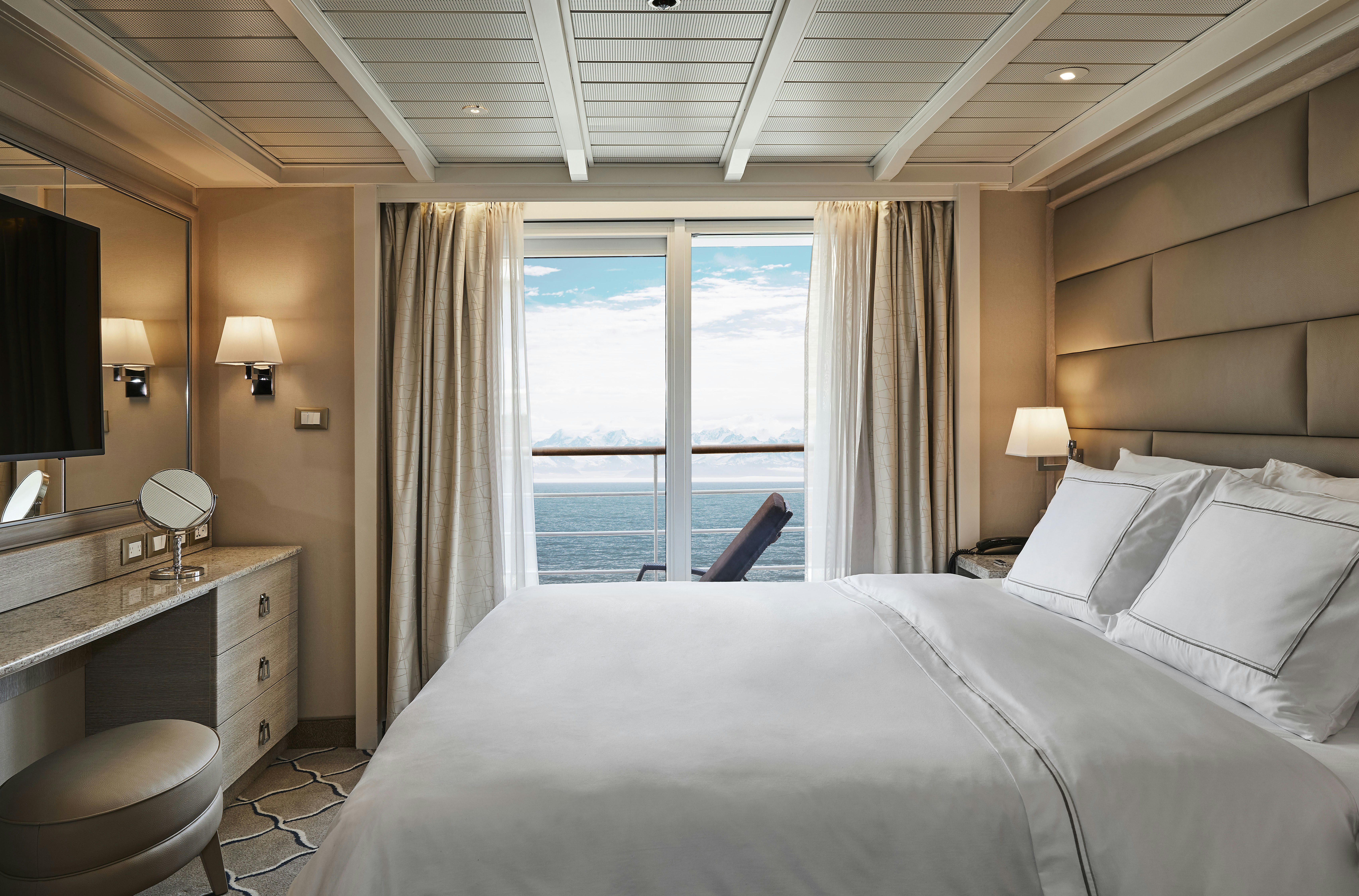 A bedroom on a cruise ship with a deck offering views of a snowcapped mountains and icy ocean.
