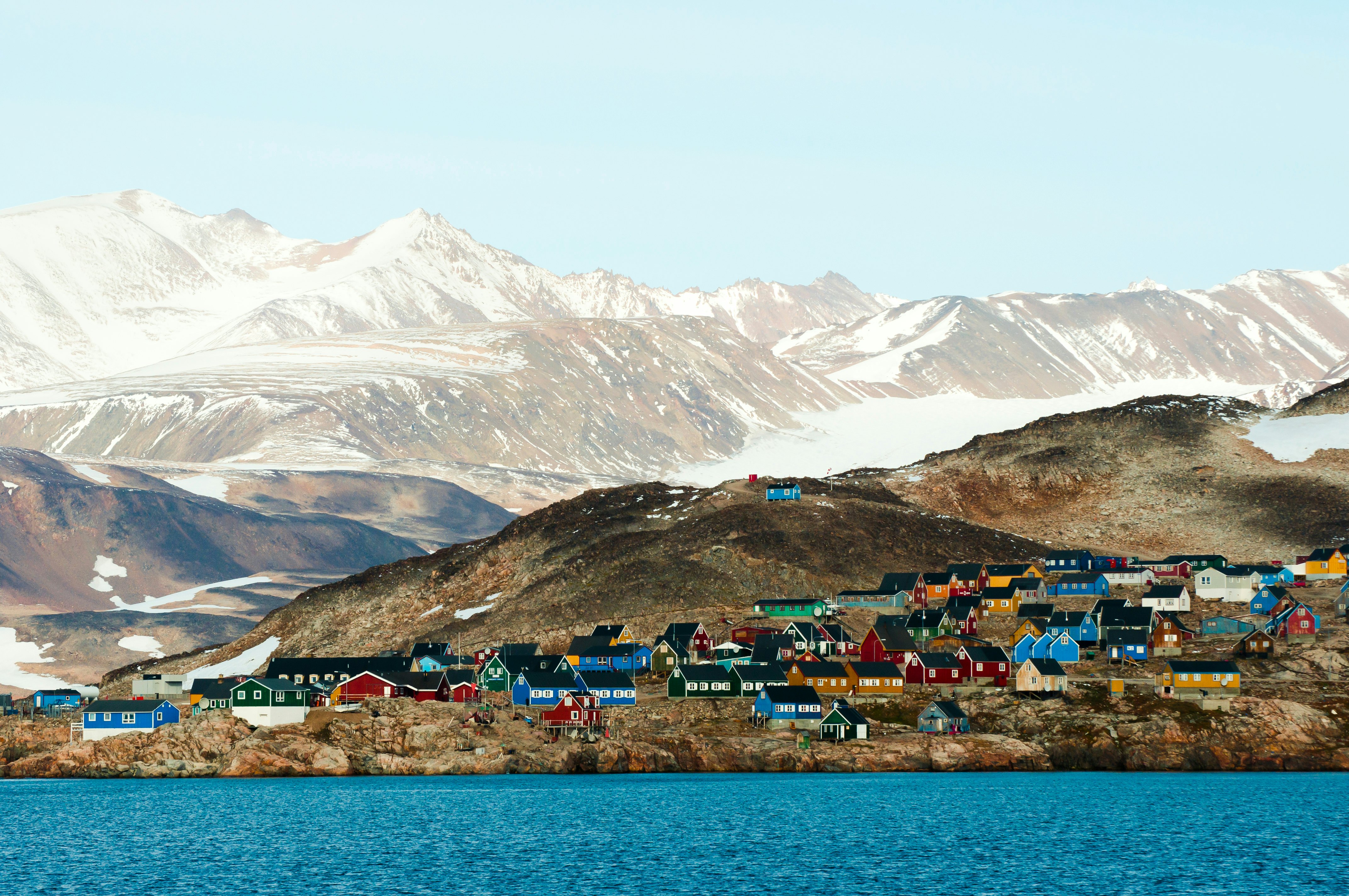 A series of small wooden houses painted in bright colors between the ocean and snow-capped mountains.