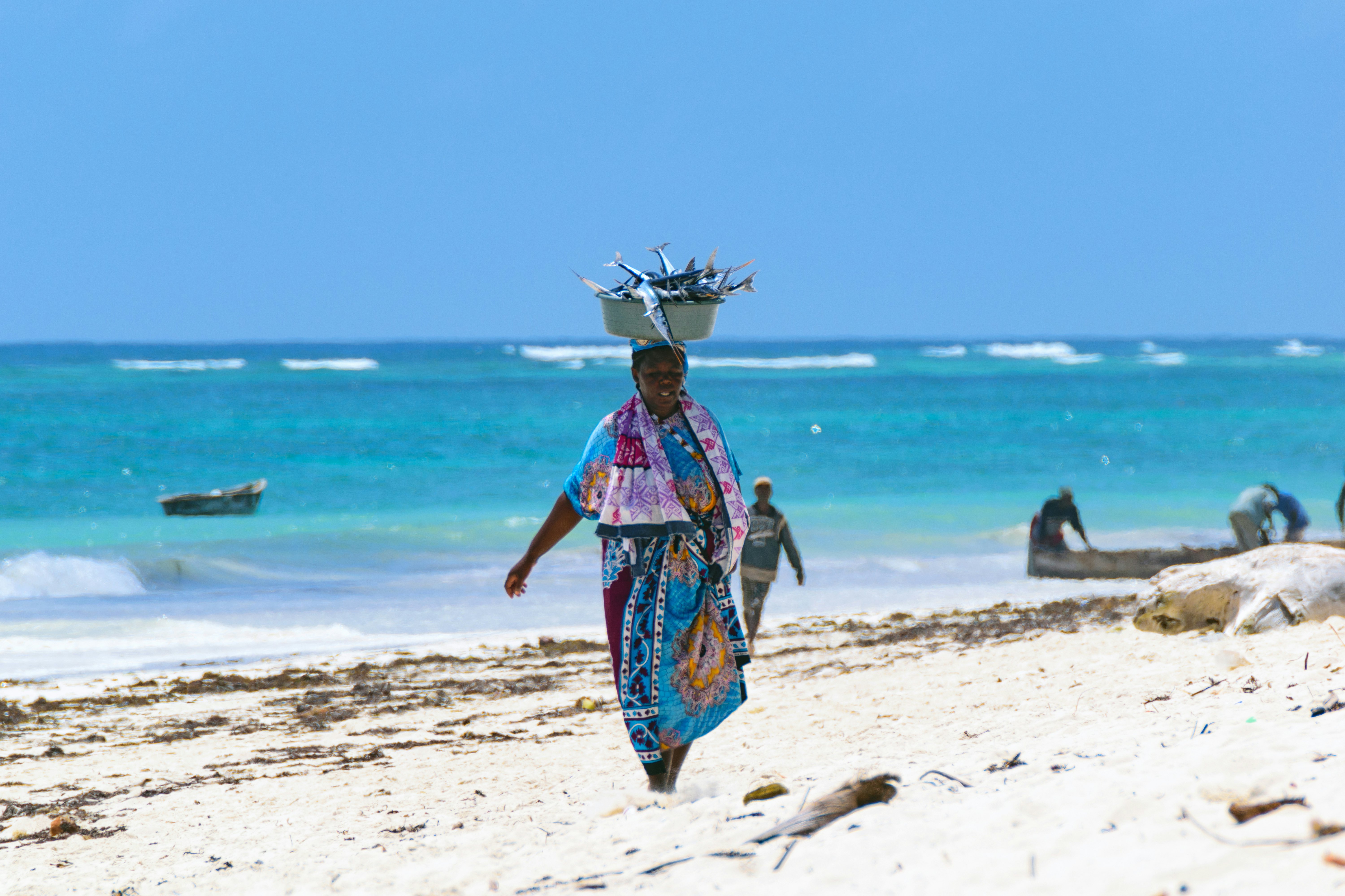 Woman walking with a basket of fish balanced on her head on Diani Beach, Mombasa, Kenya.