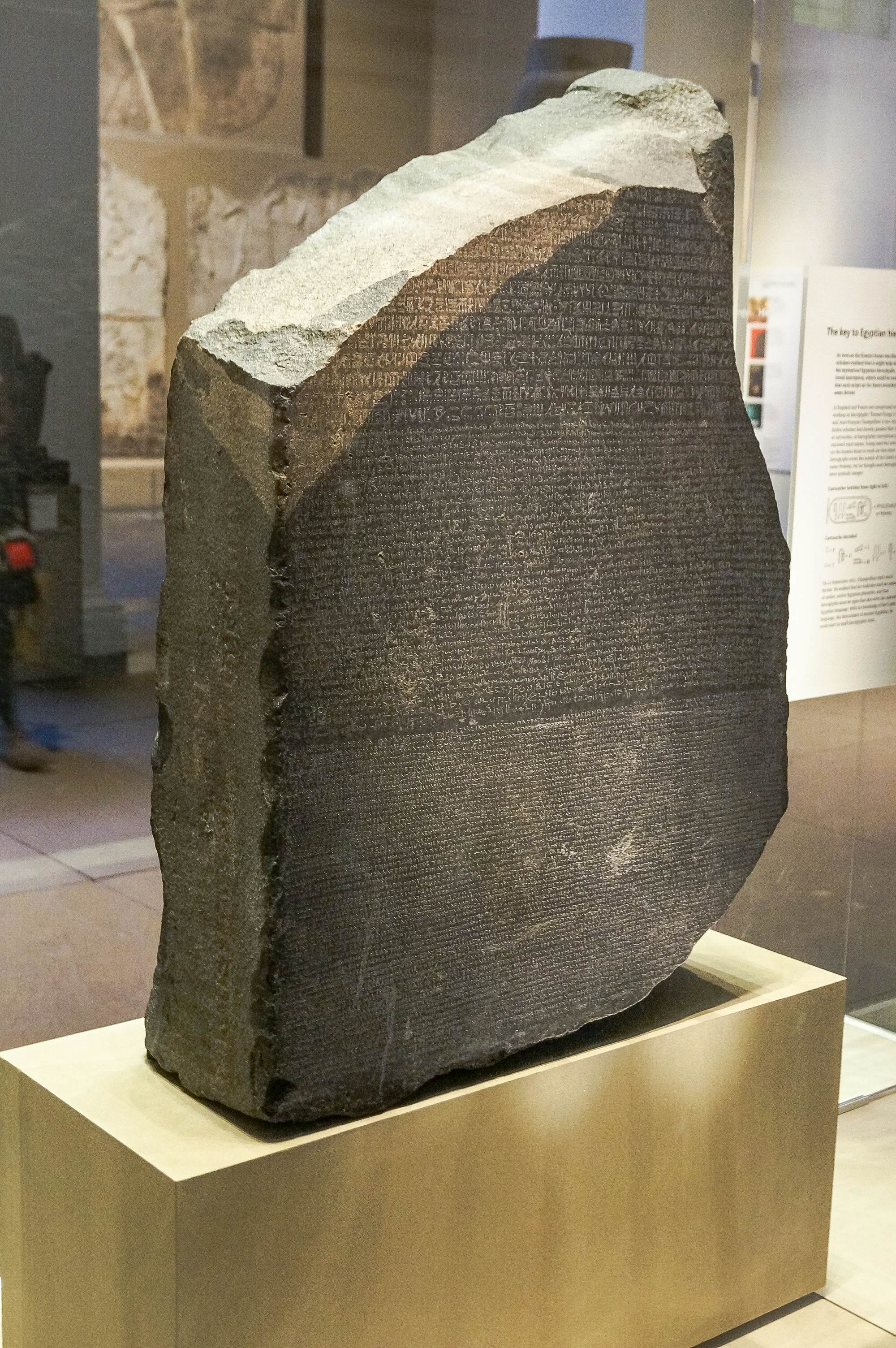 A stone tablet with writing is displayed on a pedestal at a museum in London.