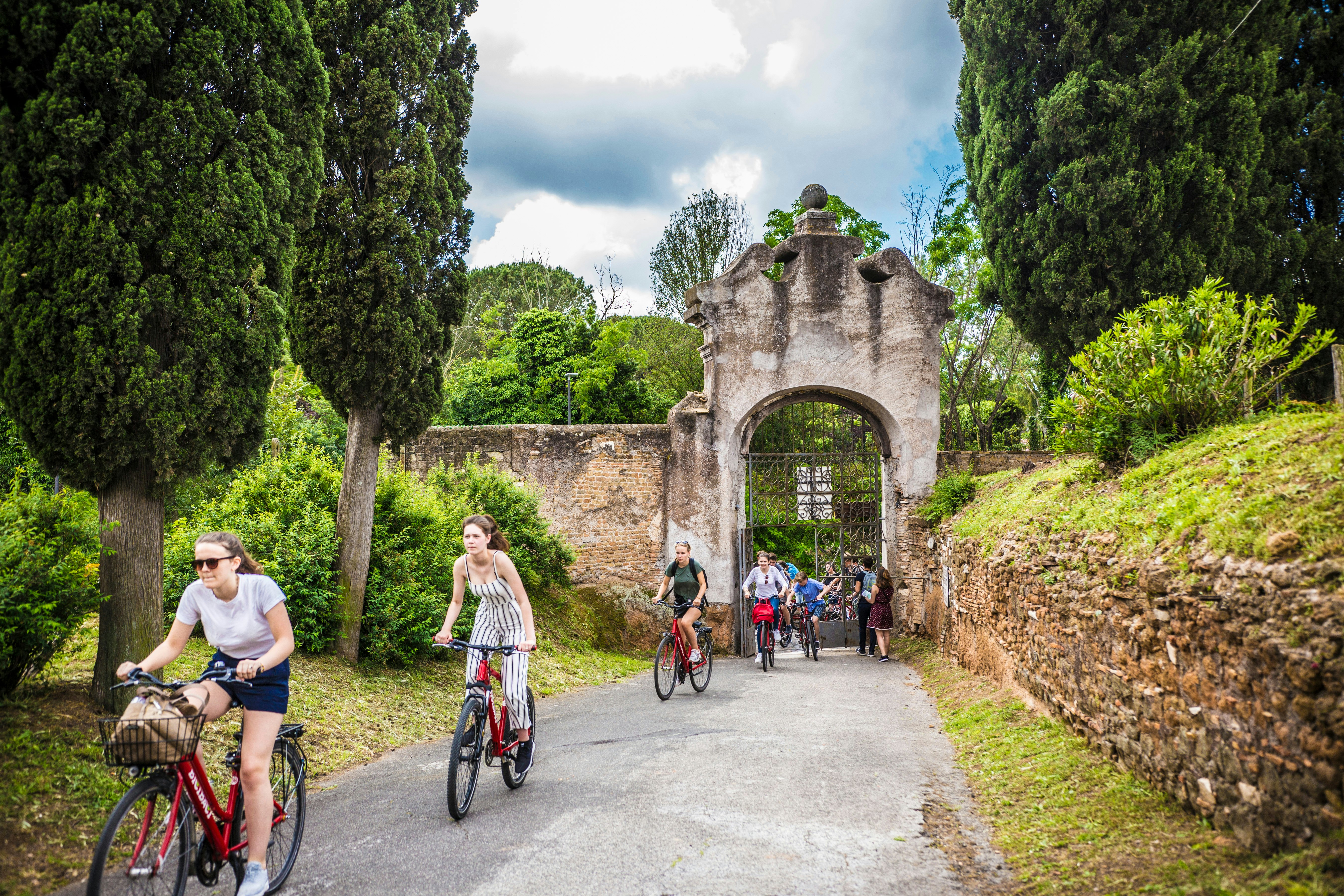 People cycle through an iron gate that opens into a garden area.