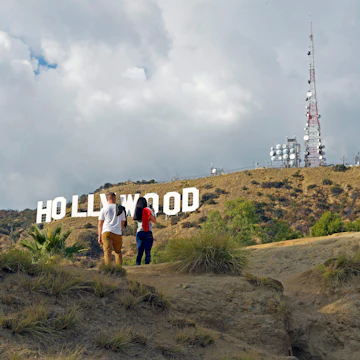 Hollywood, California/ USA 11-21-19 Two young people hiking in Hollywood California's Griffith Park stop to admire a famous sign in the Hollywood Hills License Type: media Download Time: 2024-01-17T14:24:34.000Z User: bhealy950 Is Editorial: Yes purchase_order: