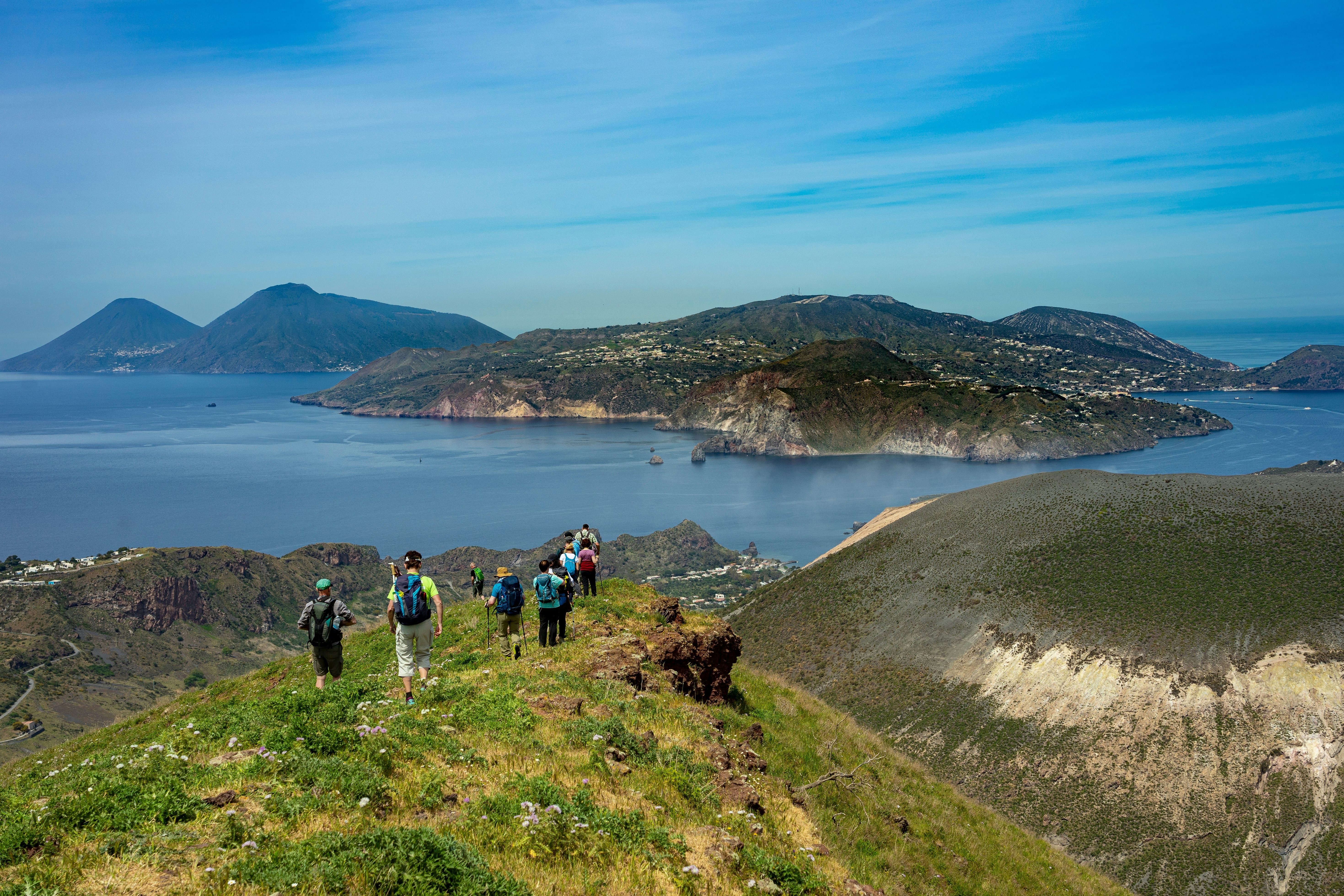 A group of hikers walk through a mountain meadow heading down towards the coastline.