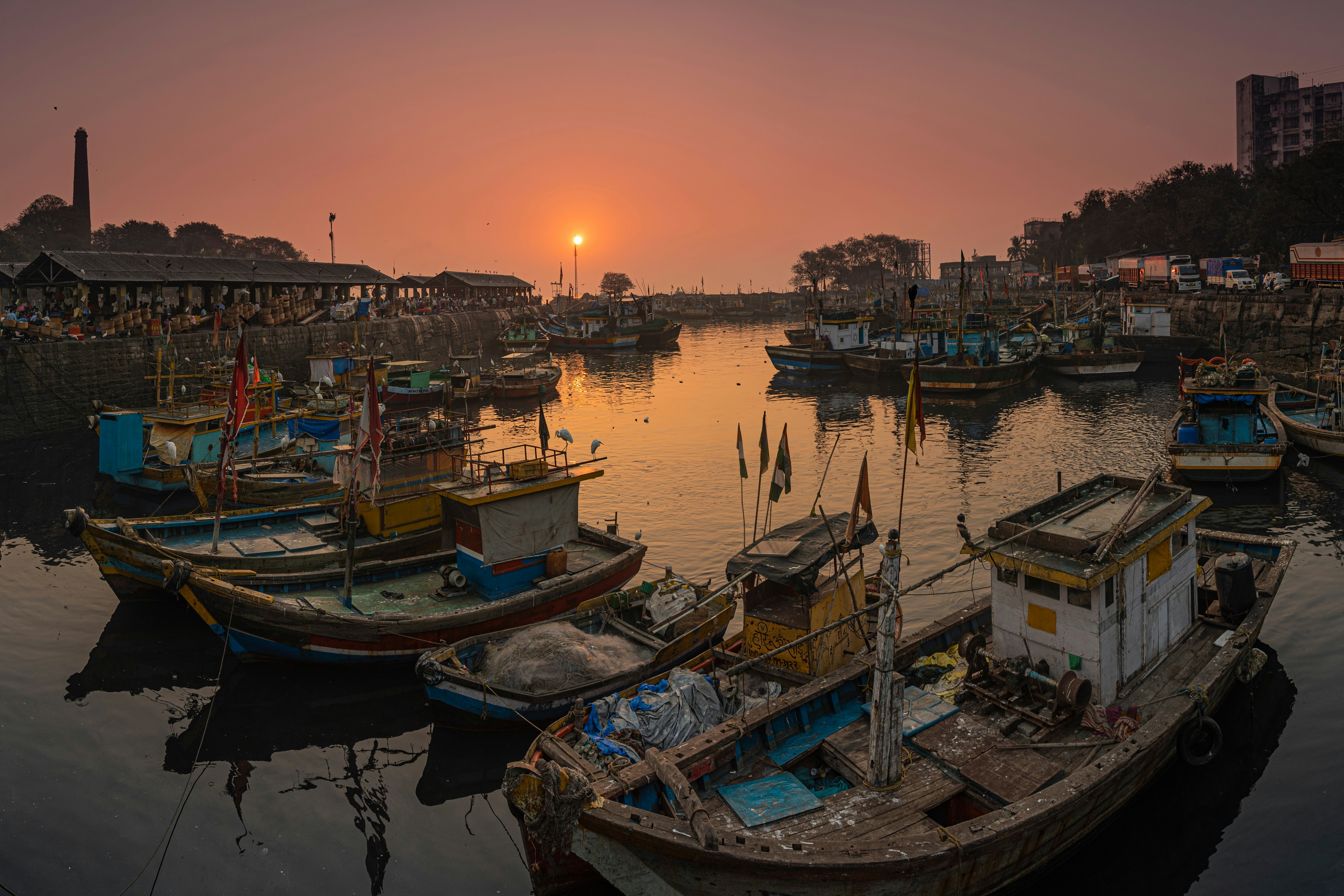 Many wooden fishing boats docked together in a small harbor at sunset.