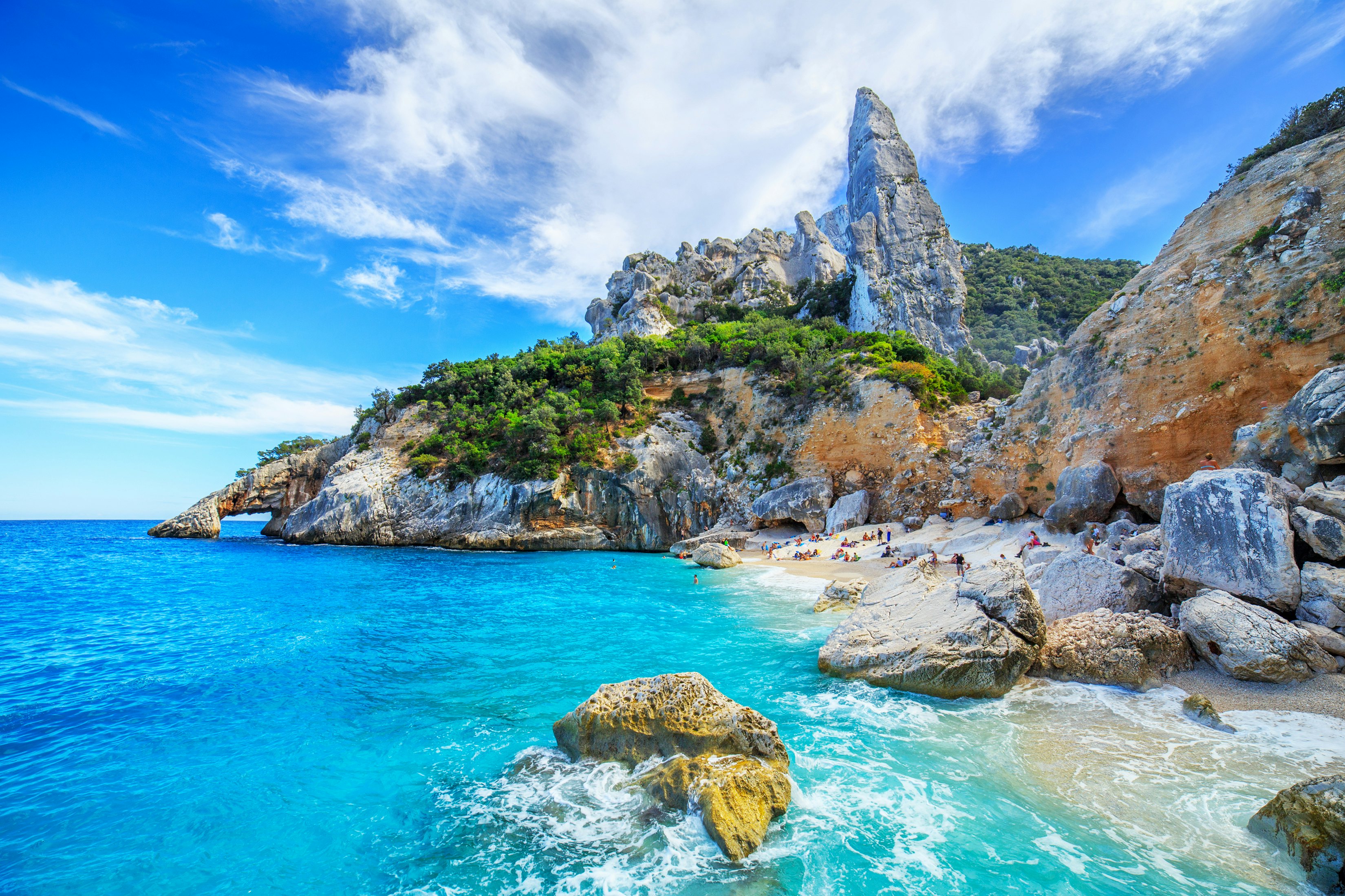 A tiny sandy beach tucked among rocky cliffs is lapped by turquoise ocean.