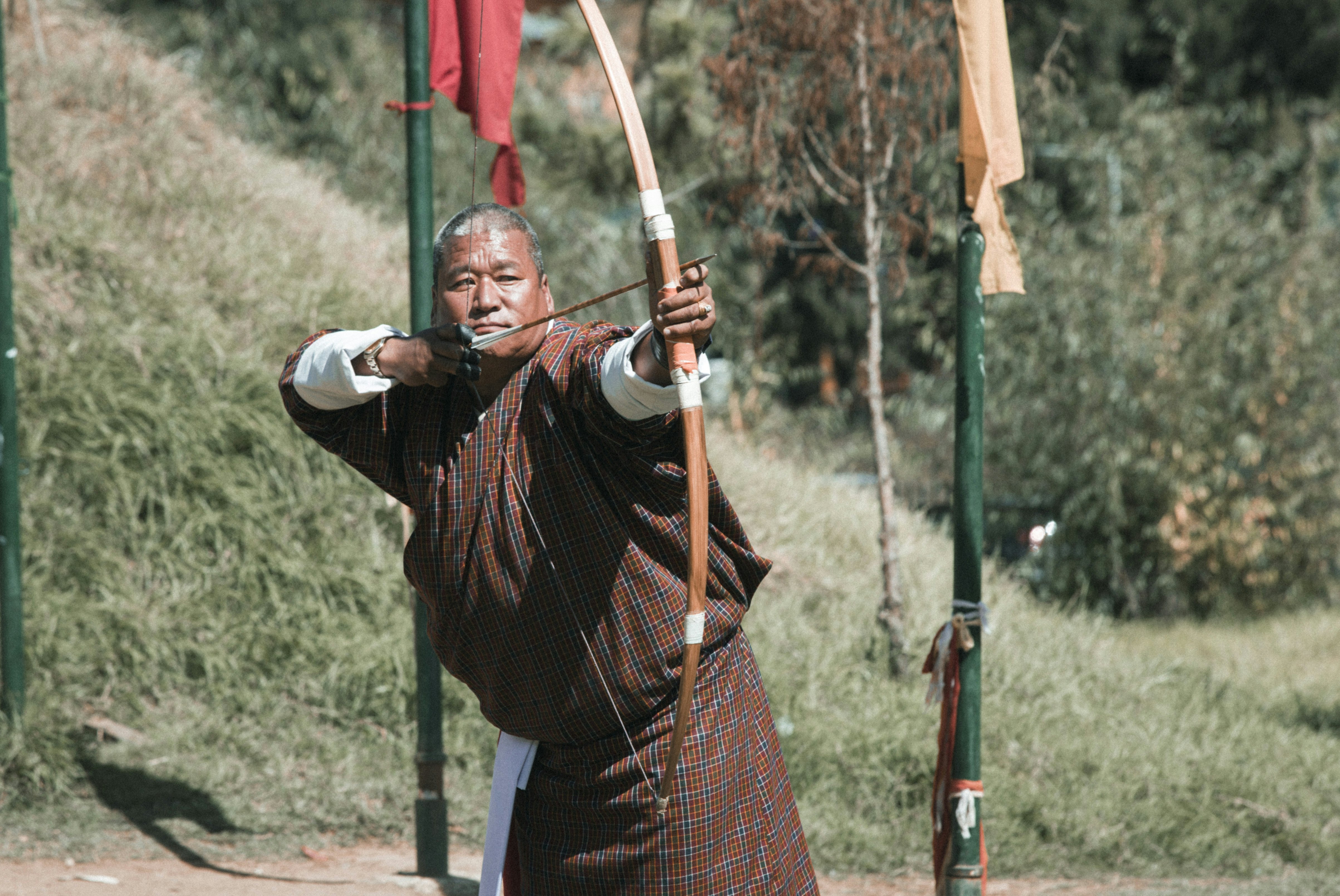 A man outdoors with a bow and arrow, presumably looking toward a target