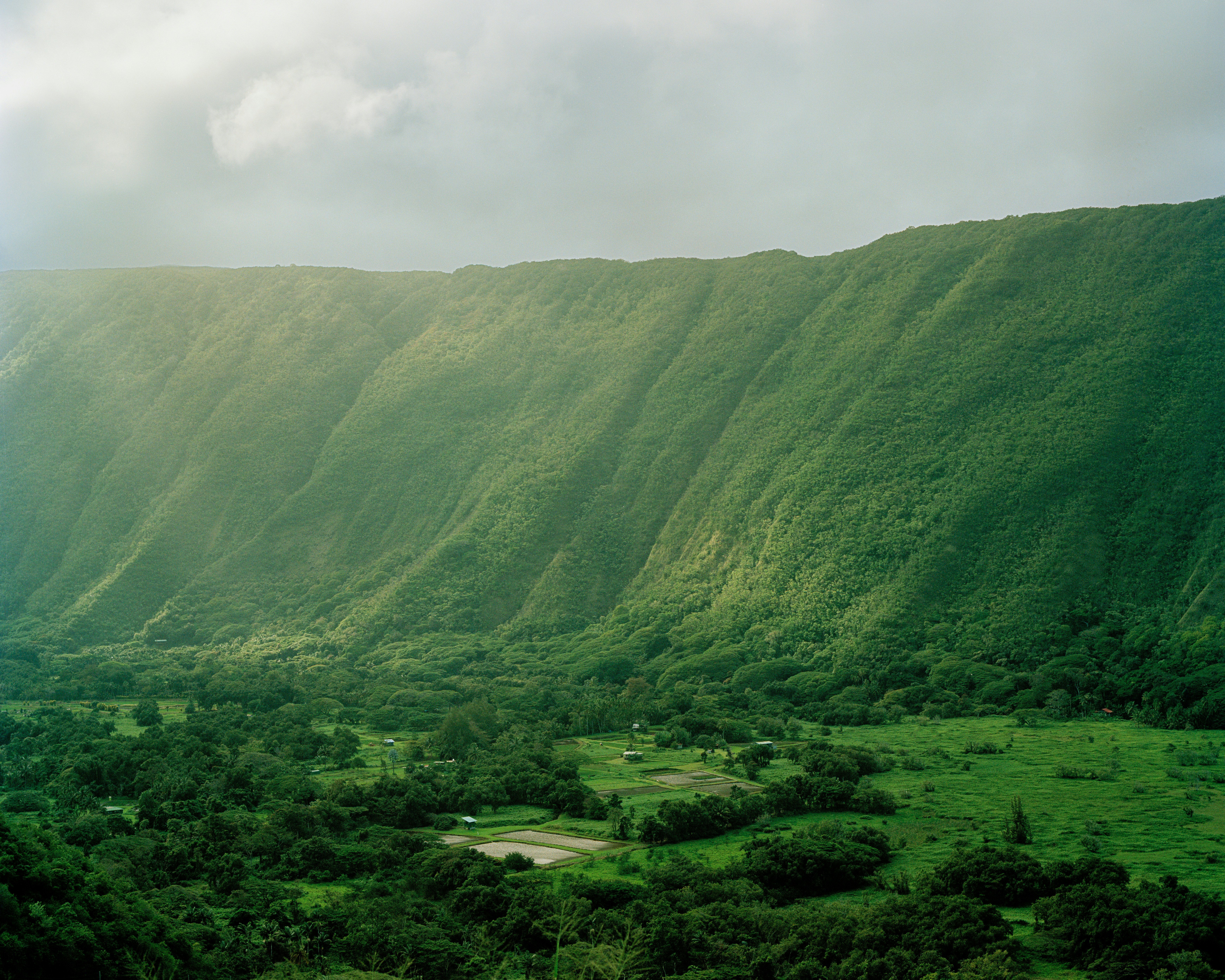Misty clouds and sunlight spill over a green ridge on Hawai'i.