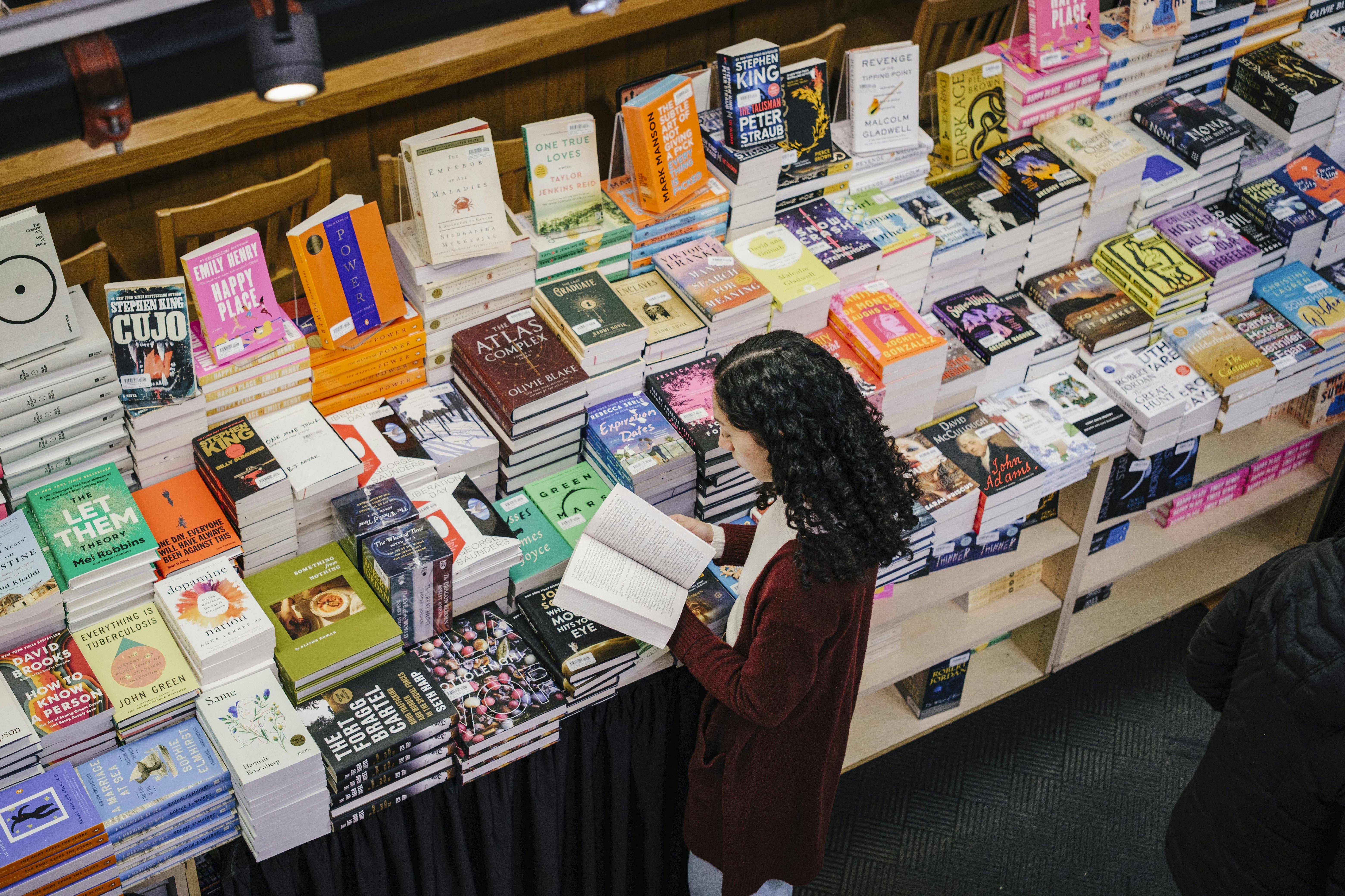 A woman leafs through a paperback at a display piled high with books for sale at a bookshop.