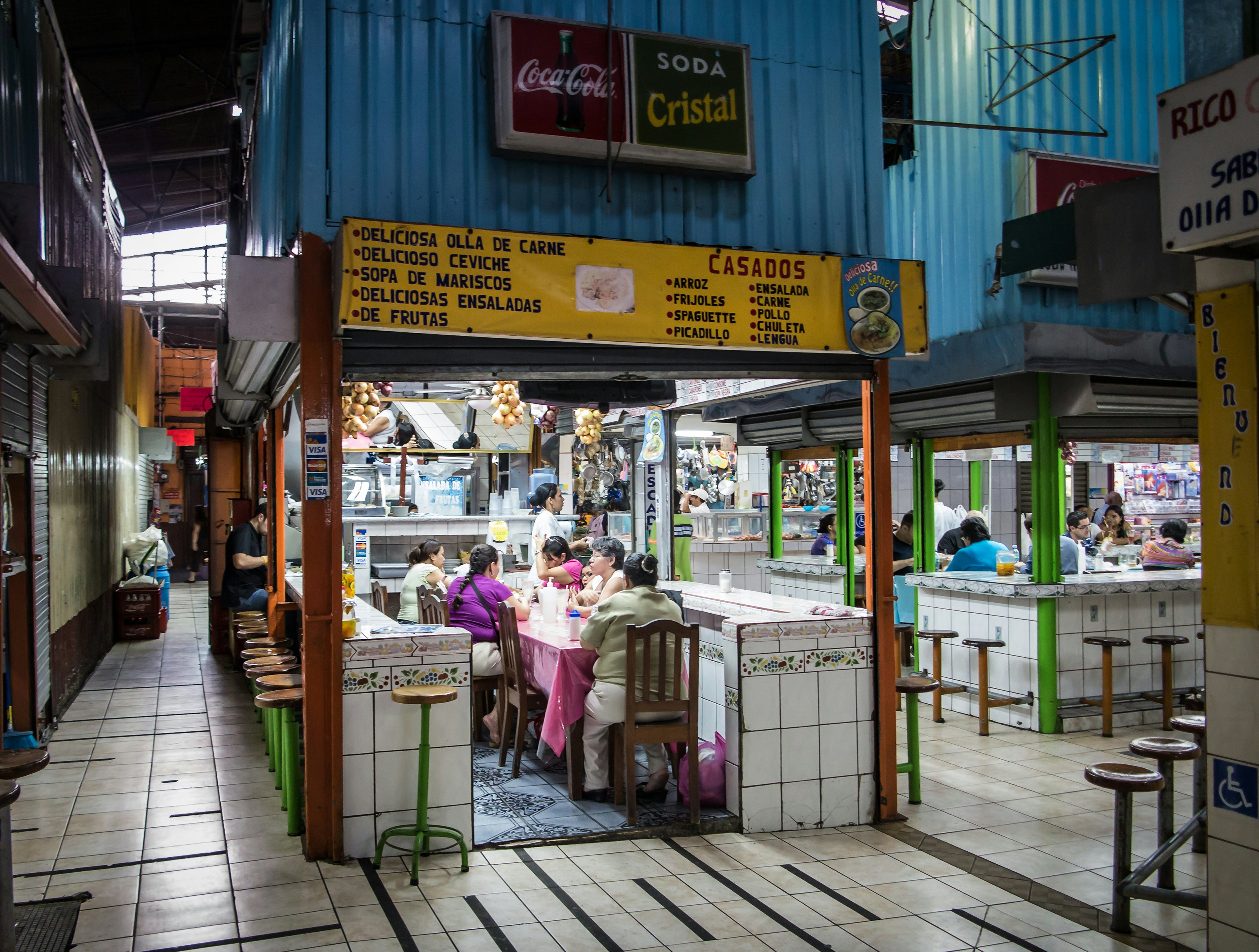 People dine at small food stalls in an enclosed market.