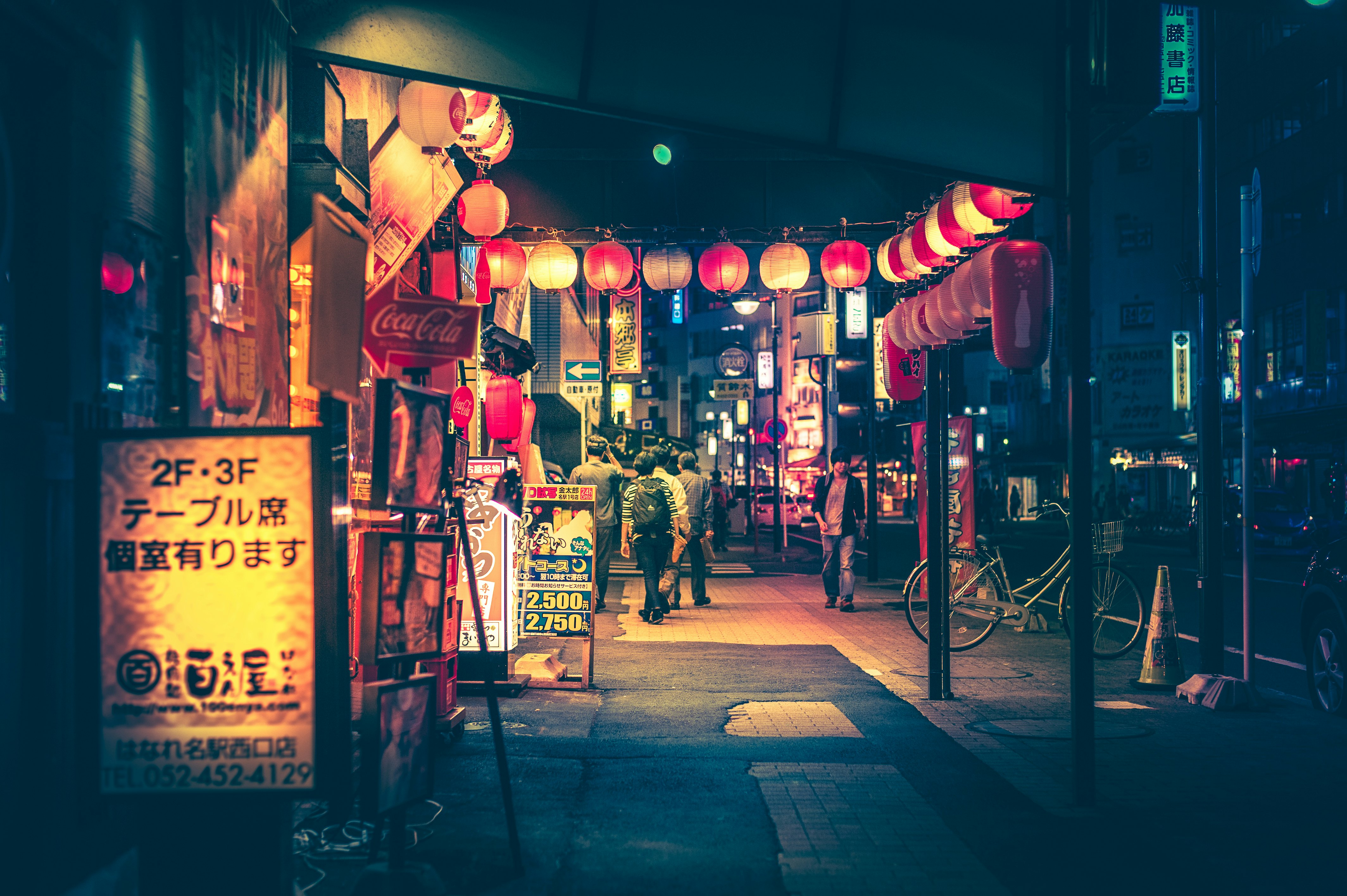 A street at night lined with bars and restaurants and decorated with glowing red paper lanterns.