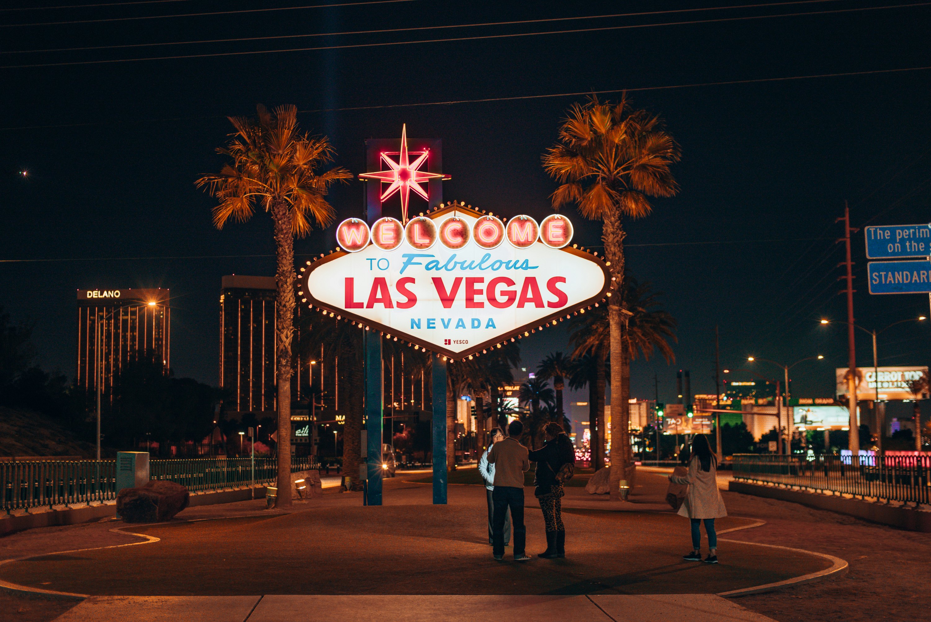 A neon side reading Welcome to Fabulous Las Vegas. It is night time and there are palm trees, buildings and people nearby.