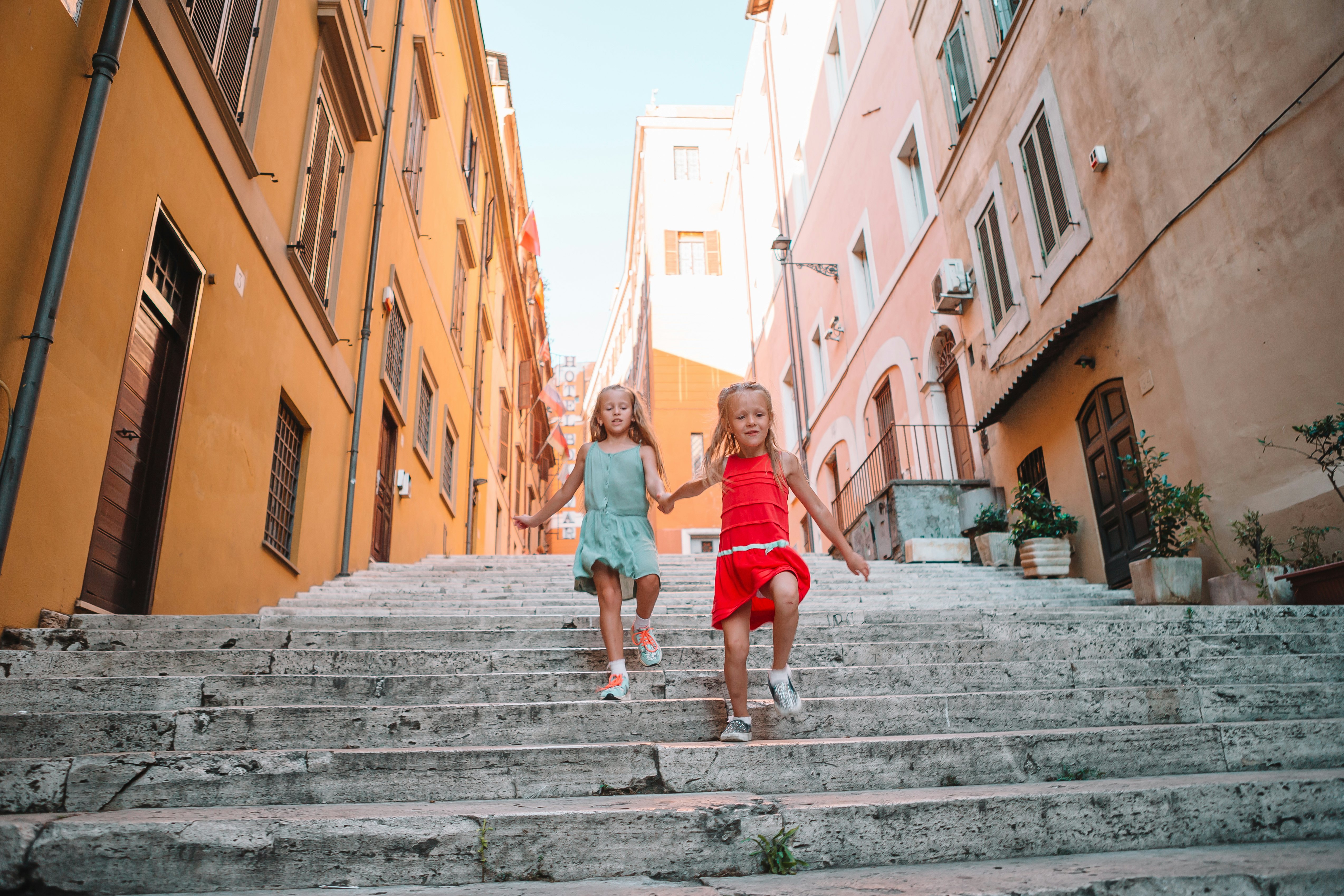 Two girls running down a set of stone steps in Rome, Italy, on a sunny day.