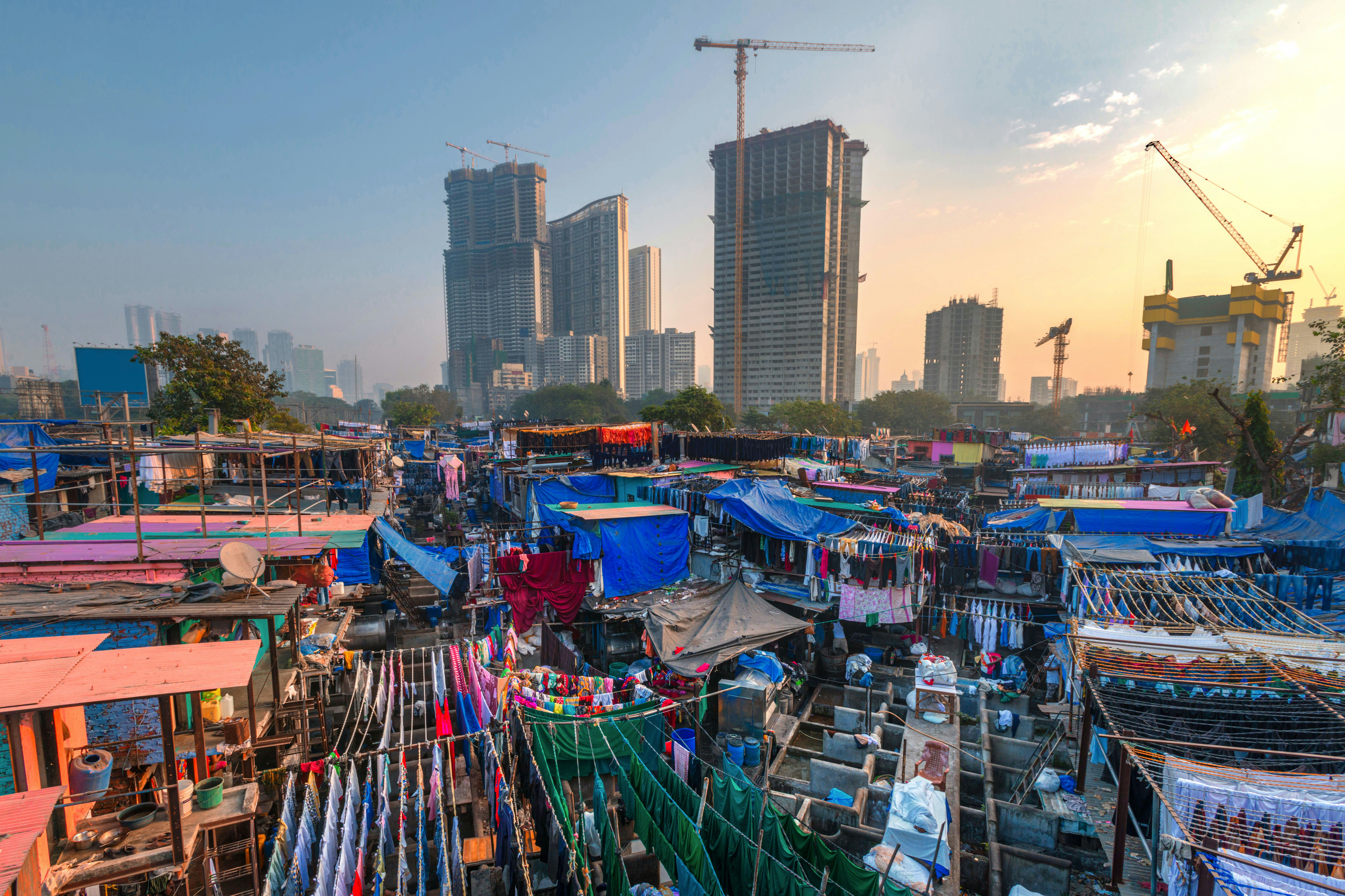 Sheets and clothes strung on washing lines in a vast outdoor laundry in the shadow of skyscrapers.