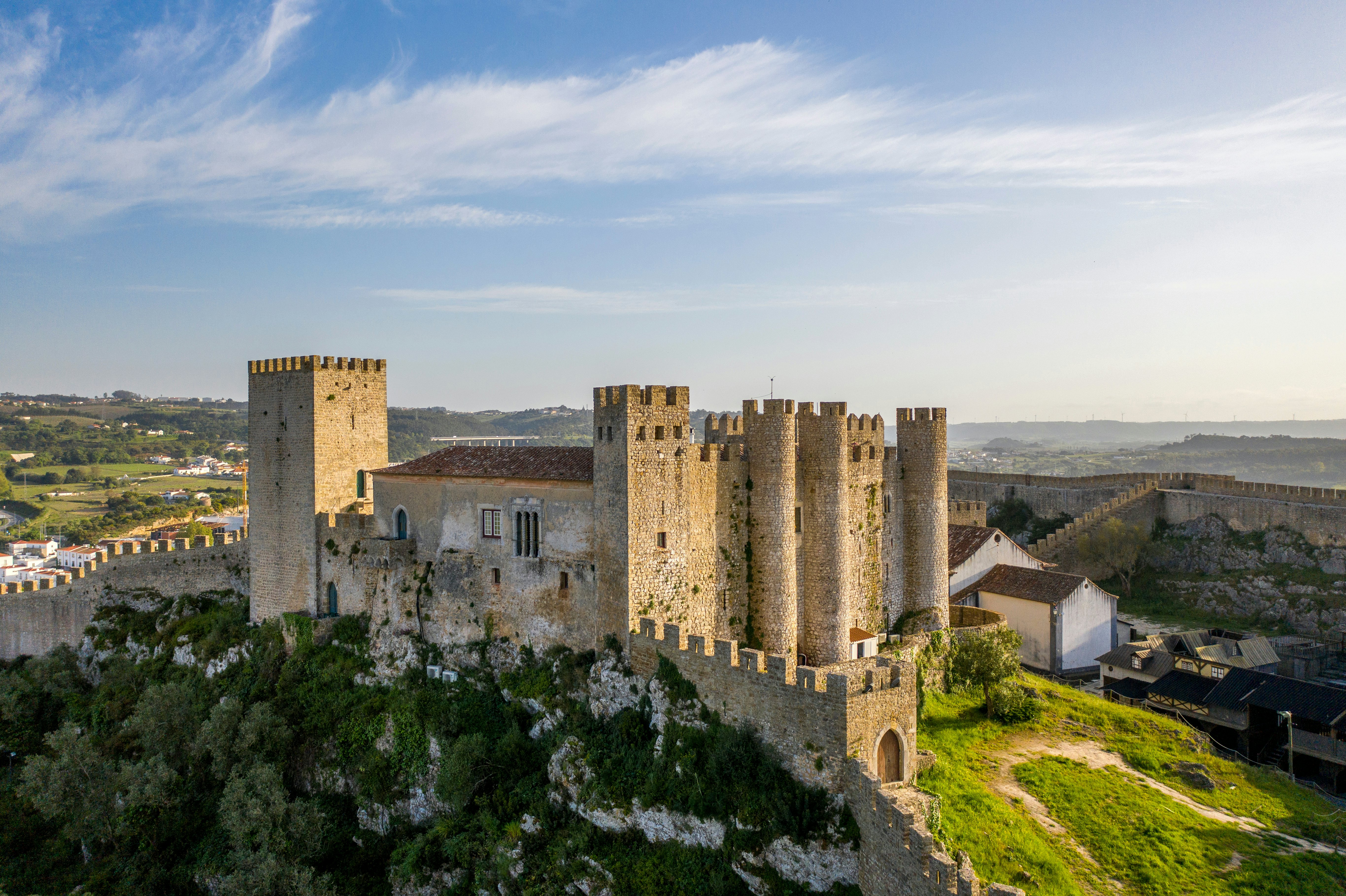 A medieval stone castle with many towers on top of a hillside; walls extend from the castle on two sides into the distance.