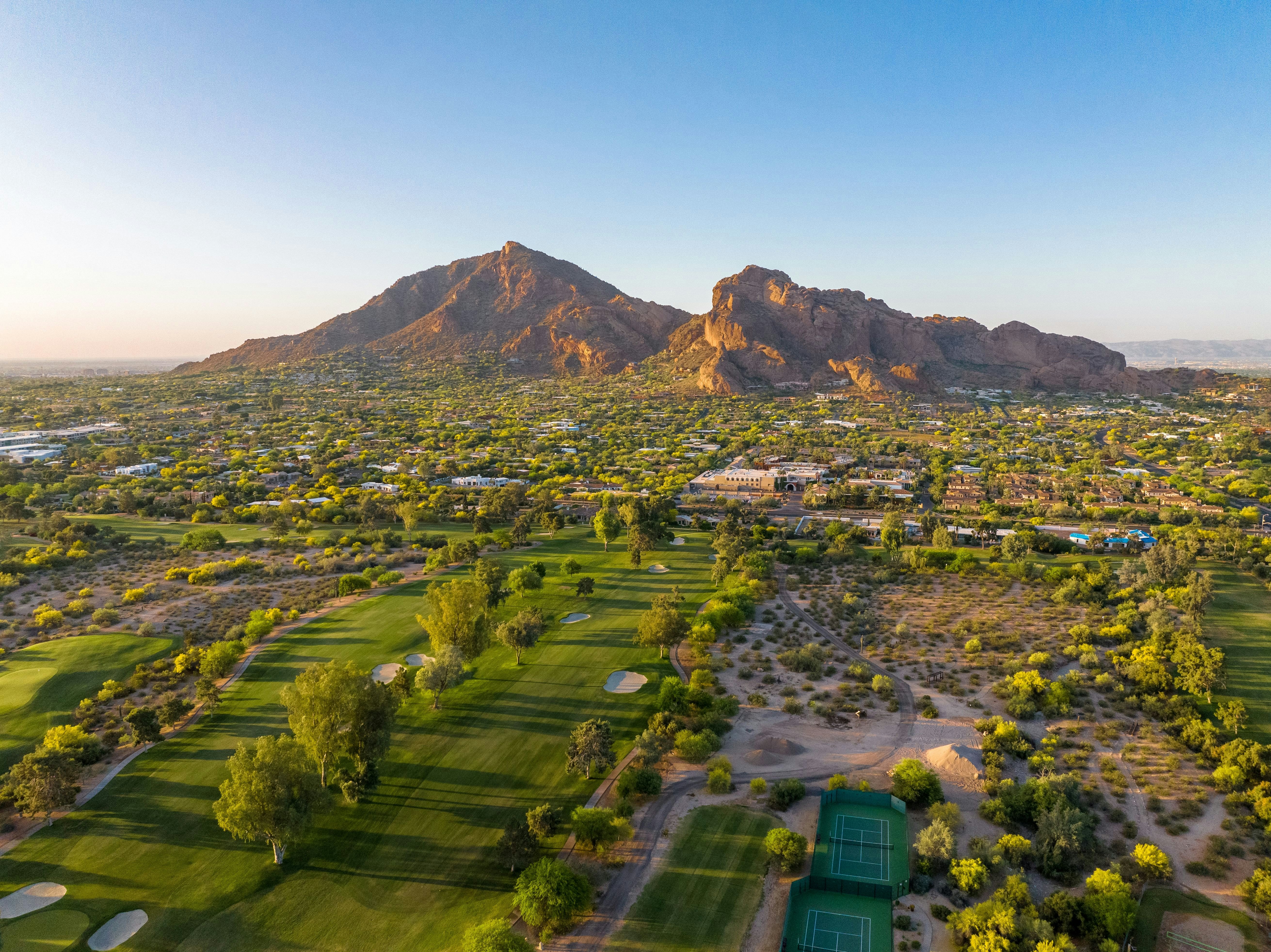 A green golf course in the foreground leads to a two-peaked rock formation in the background at sunset.
