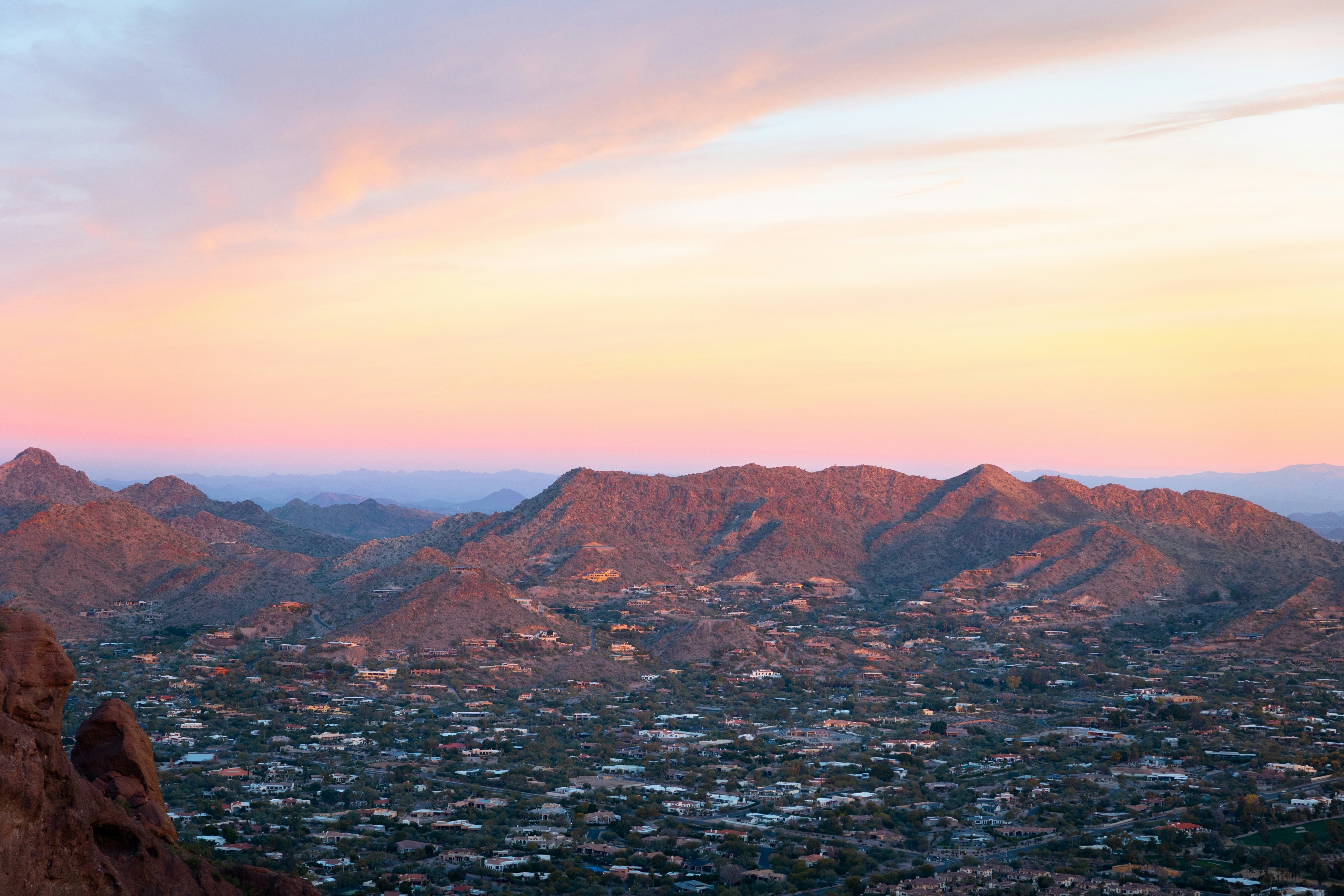 The pink light of sunrise hits the peaks of a mountain while the houses in a valley are still in shade.