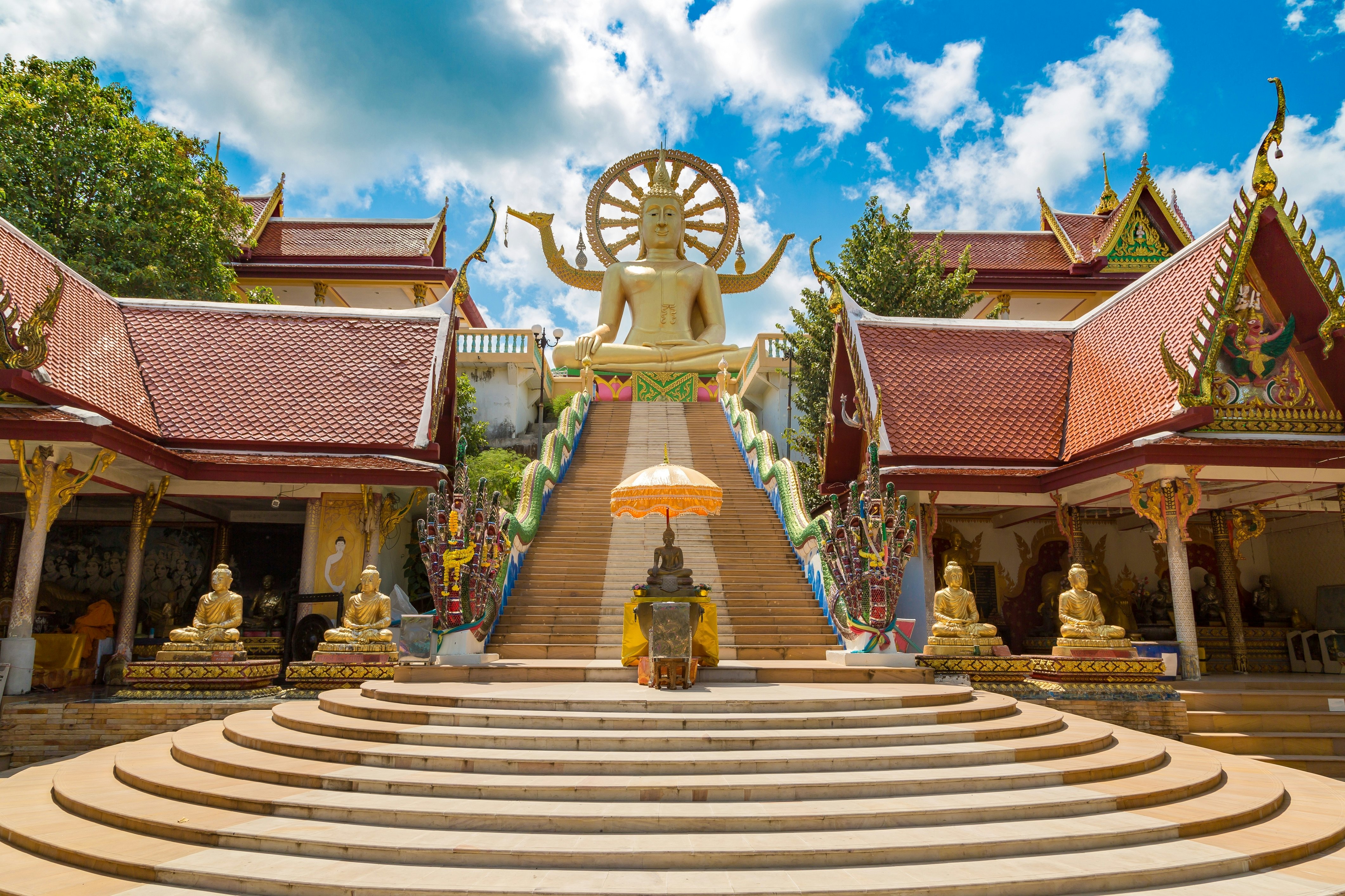 Steps in a temple complex lead upwards to a seated golden Buddha.