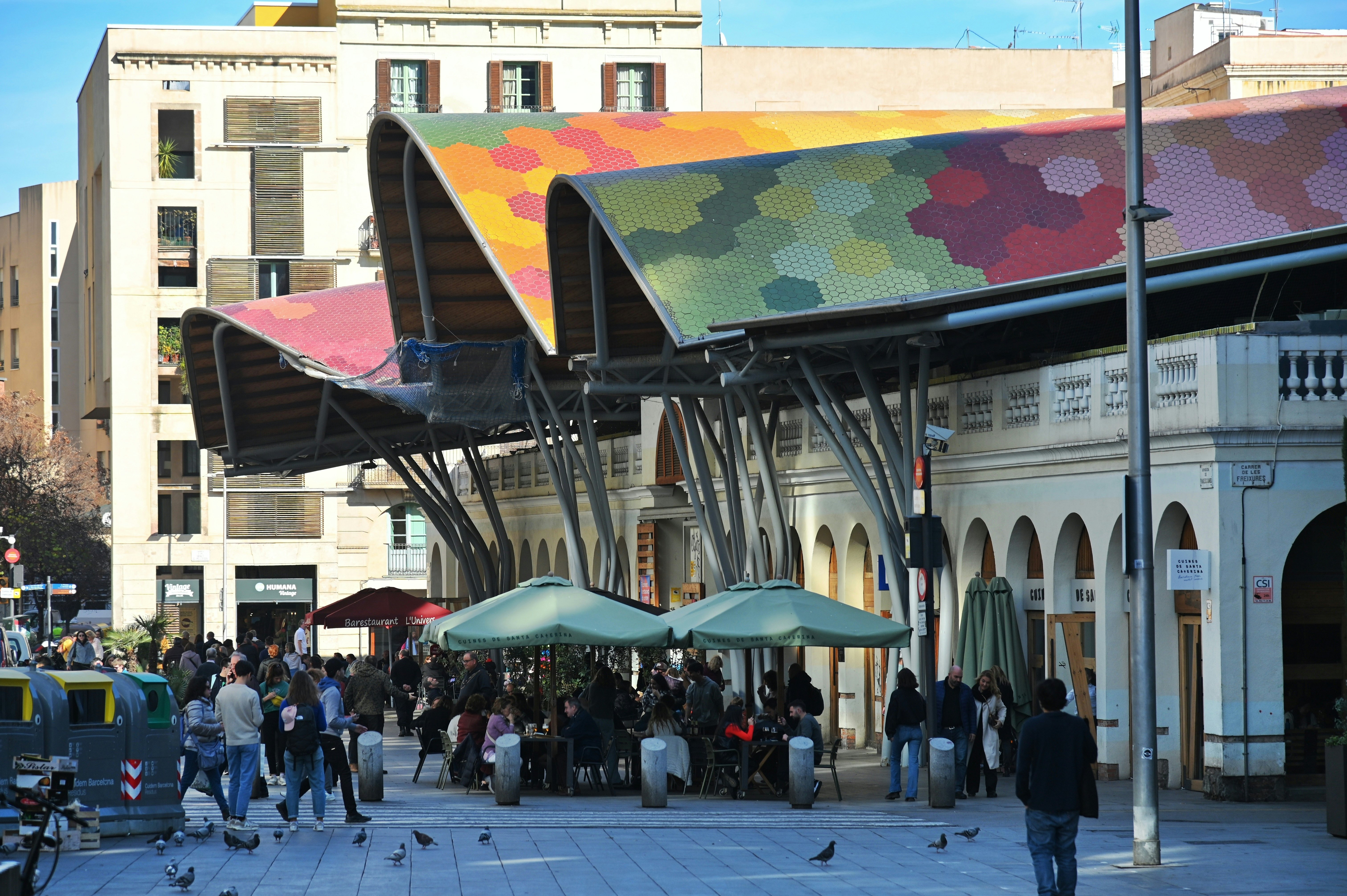 A multicolored roof curves in waves over the arched white facade of a historic building in Barcelona, Spain.