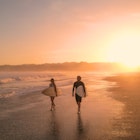 AERIAL: Cheerful surfers admire big waves while walking on sandy shore at sunset. Stunning view of orange glowing sandy beach and rolling ocean waves. Surf couple on a surf trip at exotic Playa Venao., License Type: media, Download Time: 2025-11-14T15:02:14.000Z, User: katelyn.perry_lonelyplanet, Editorial: false, purchase_order: 65050 - Digital Destinations and Articles, job: wip, client: wip, other: Katelyn Perry