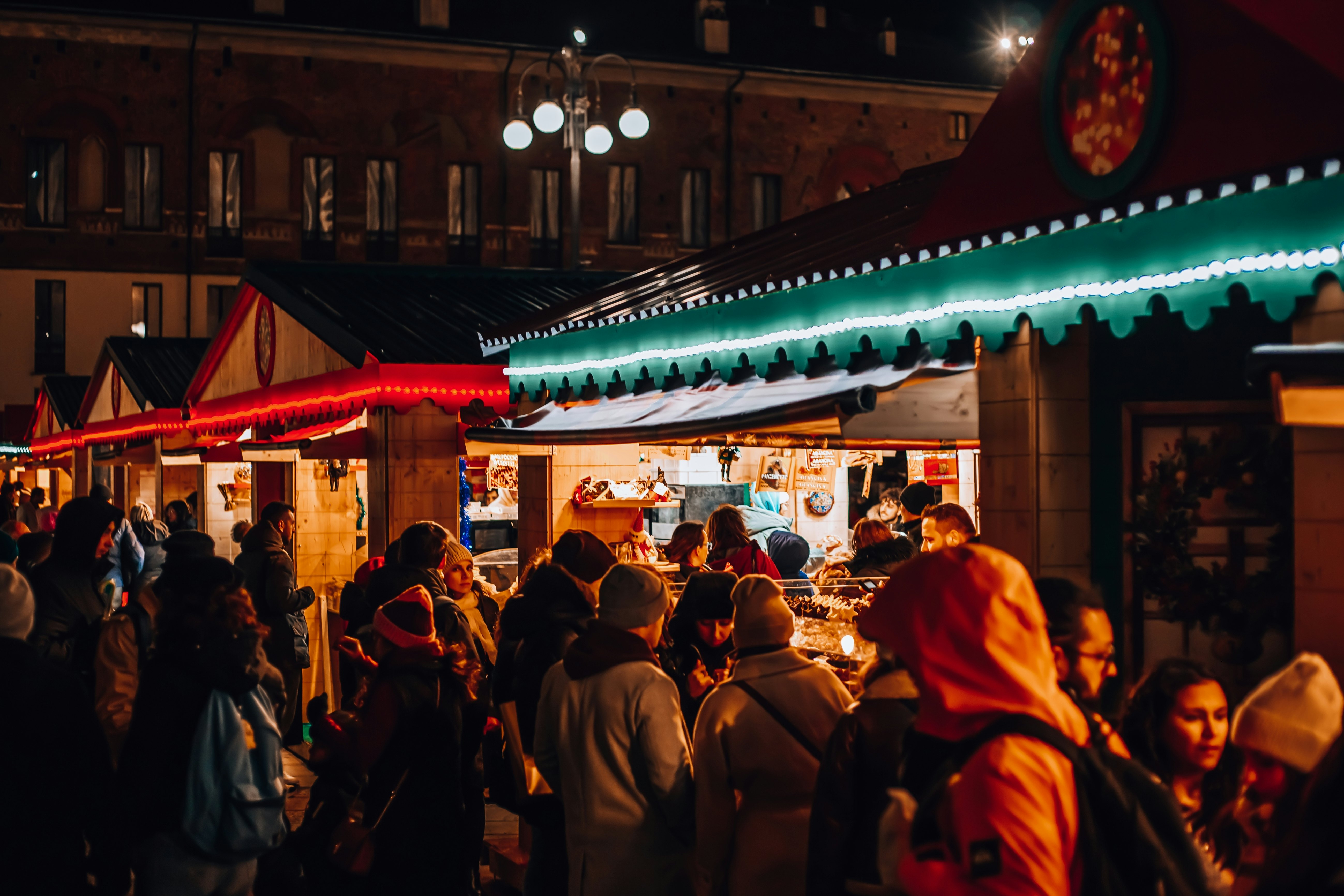 People shop at stalls at a holiday market at night in a city.