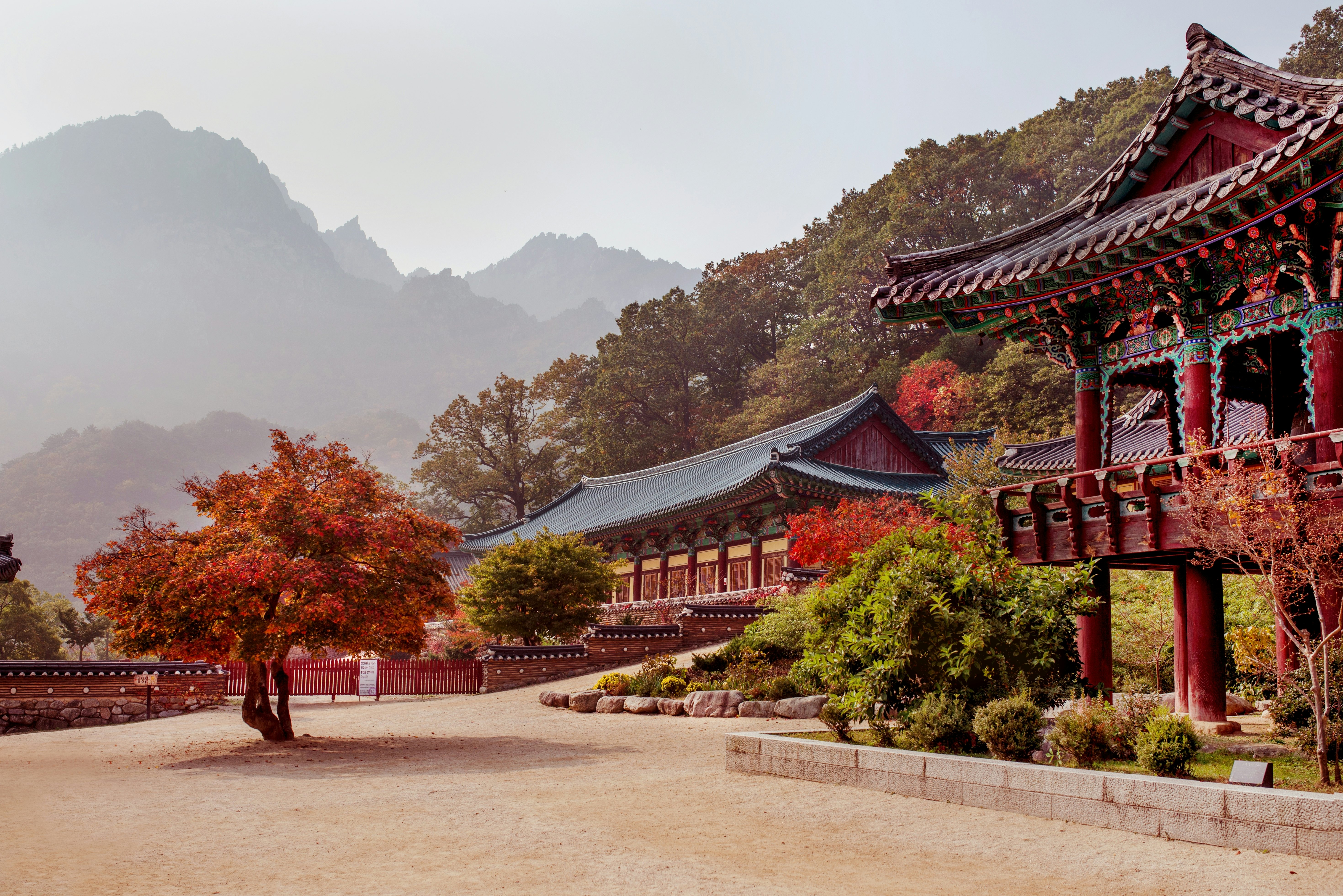 Low-rise temple buildings in a mountainous landscape surrounded by red foliage.