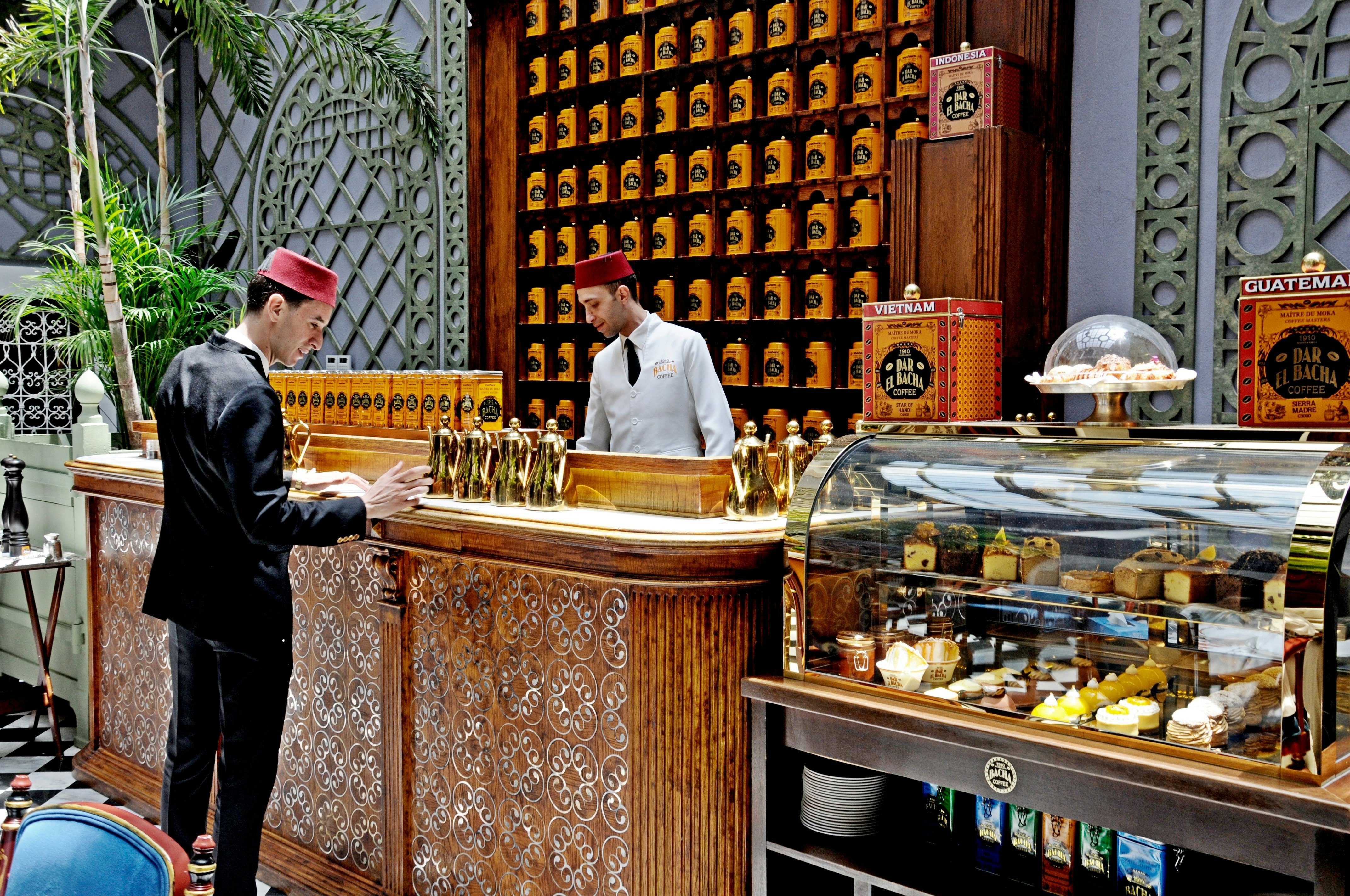 Two servers in a coffee shop with a wall of coffee beans and tiled decor.