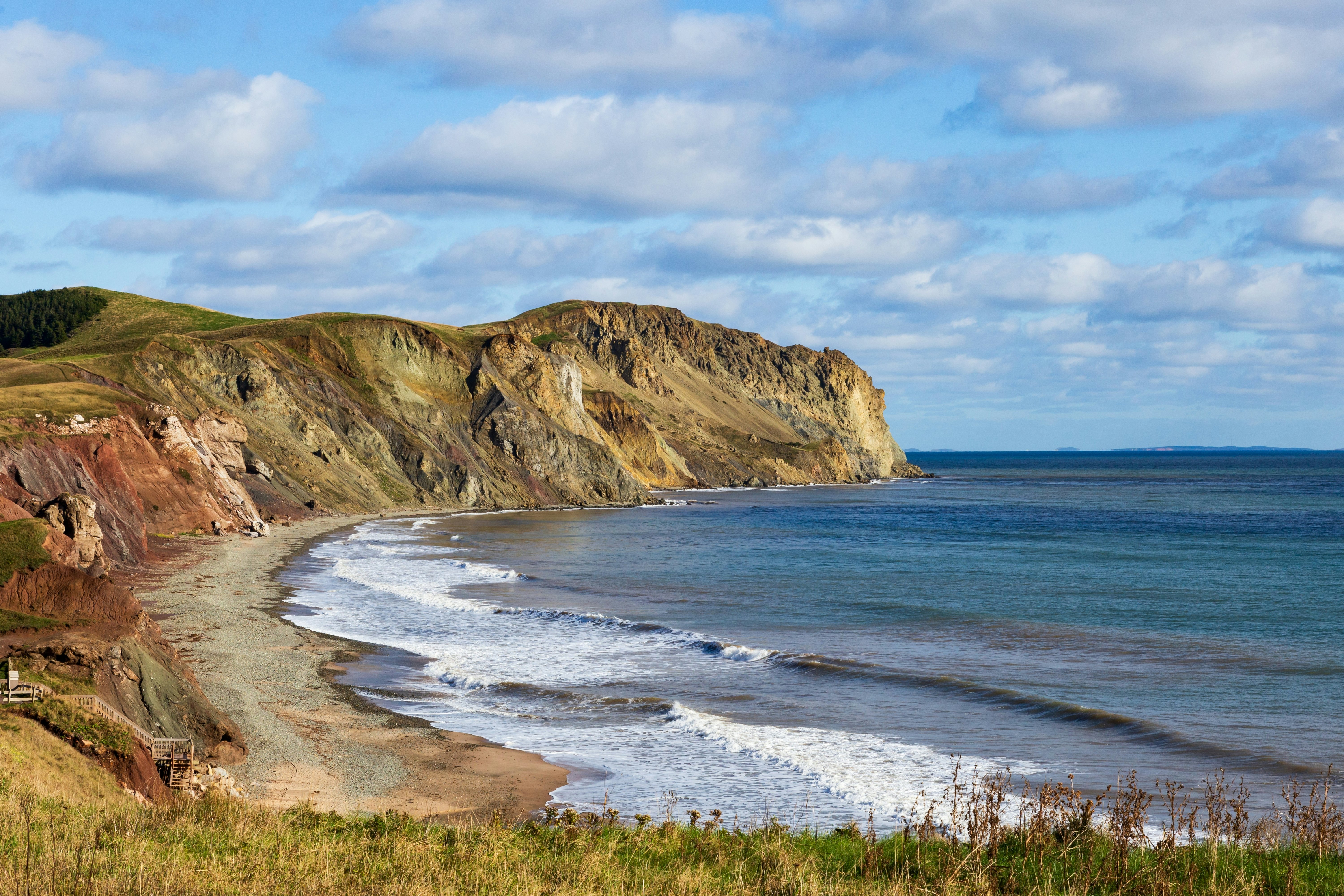 White-capped waves lap a small beach surrounded by dramatic sandstone cliffs.