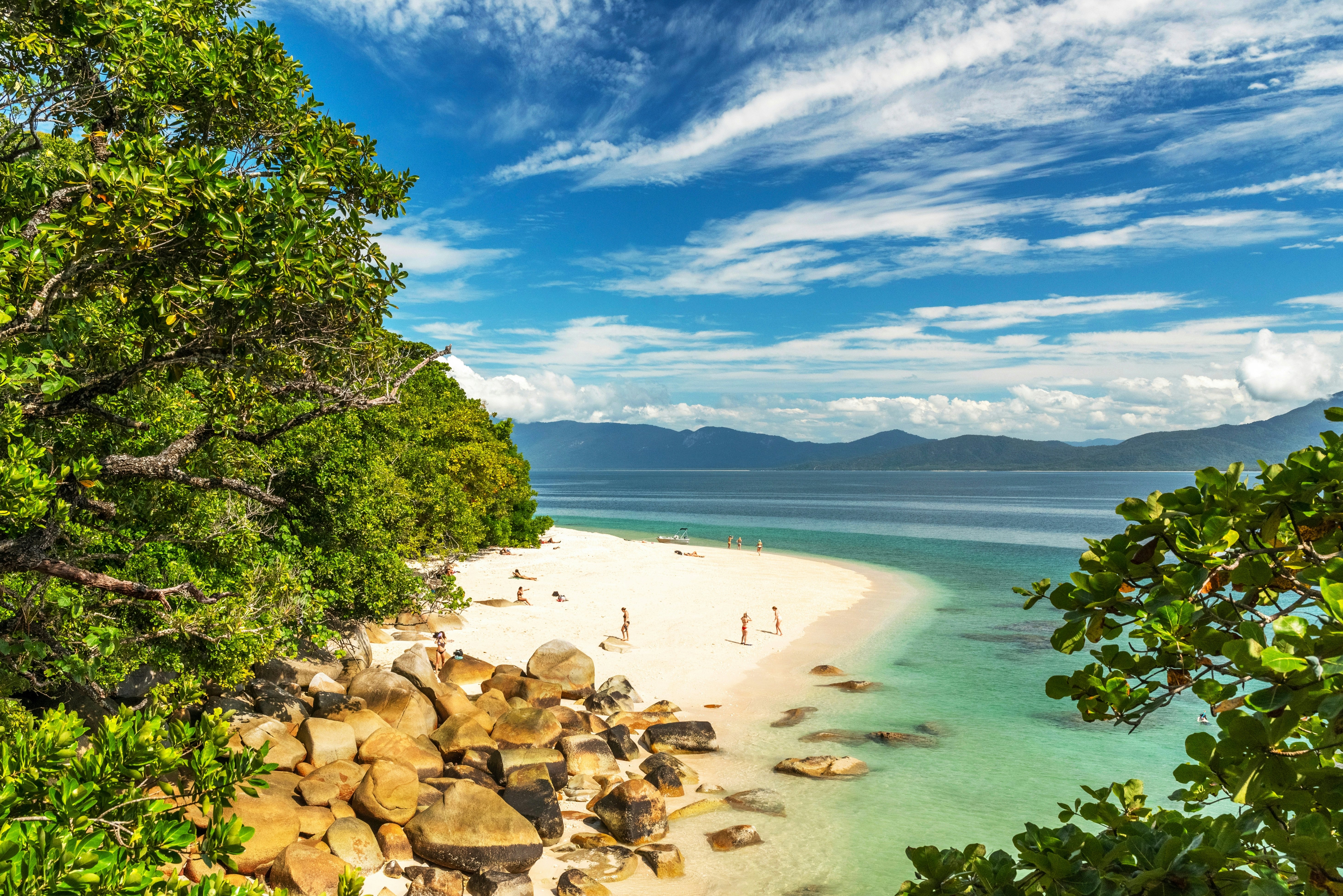 People on a white-sand beach with large boulders backed by dense tropical foliage.