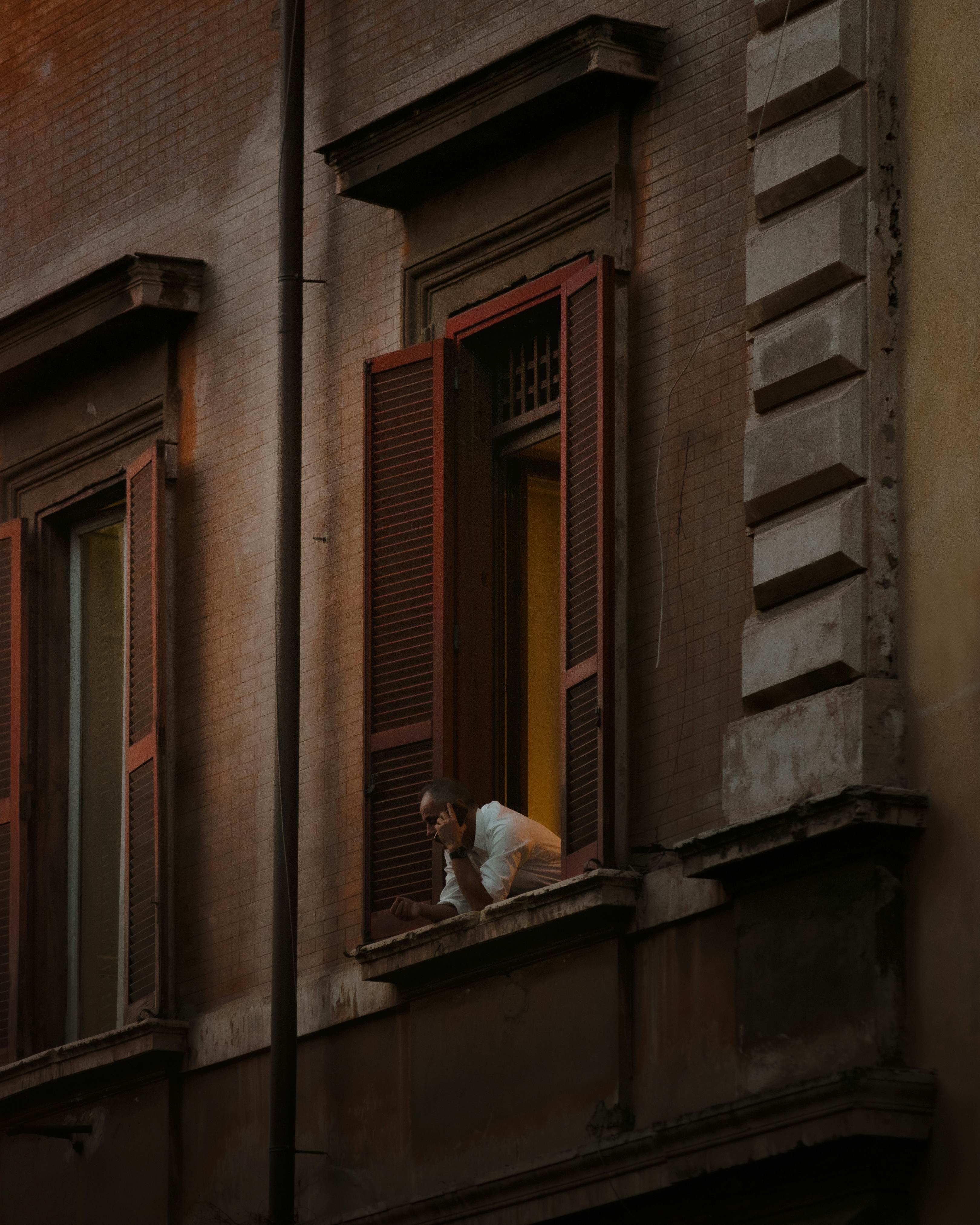 A man looks out over his open window from a typical Roman apartment building