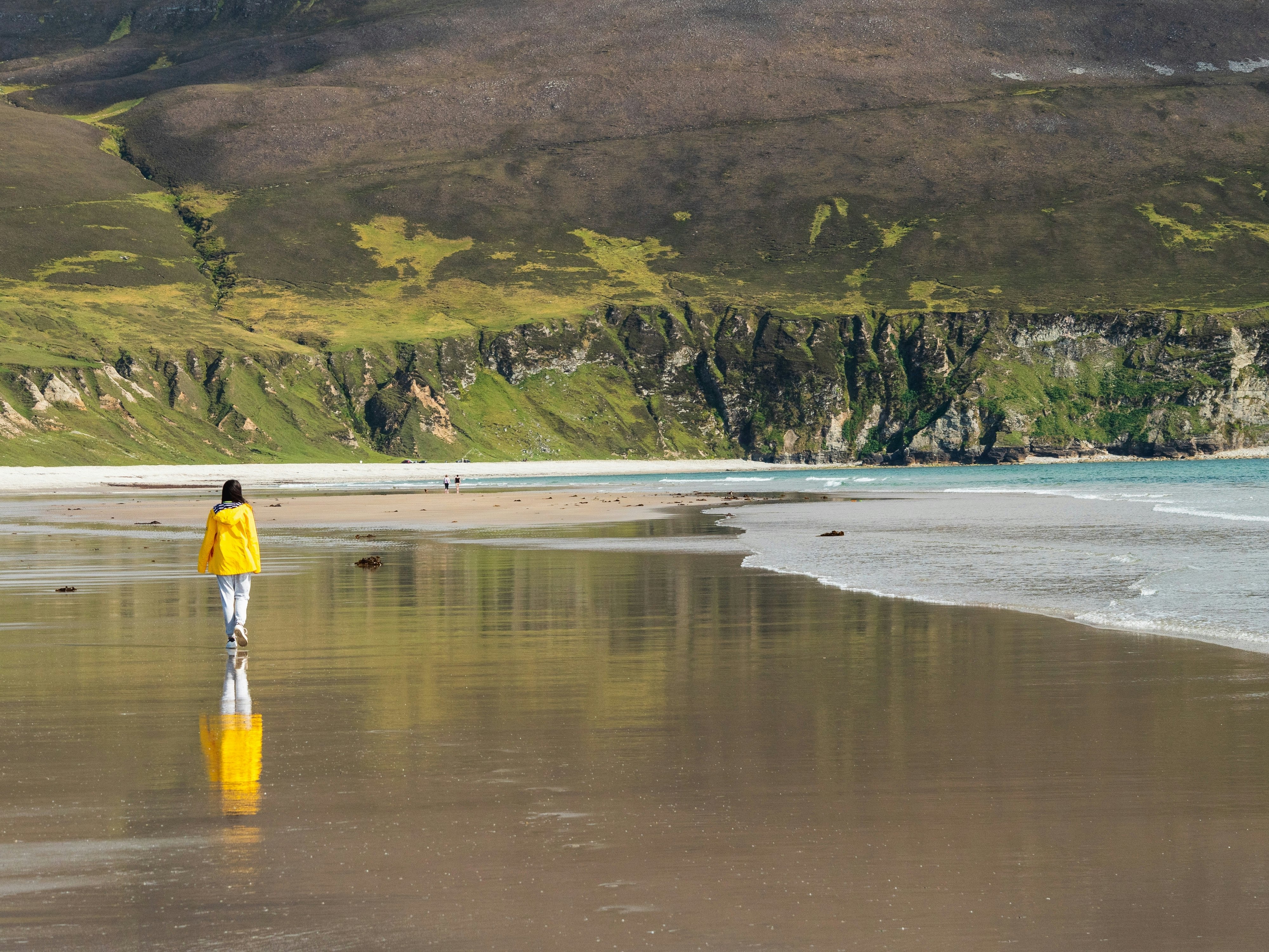 A girl in a yellow coast walking on Keel beach in Ireland at low tide.