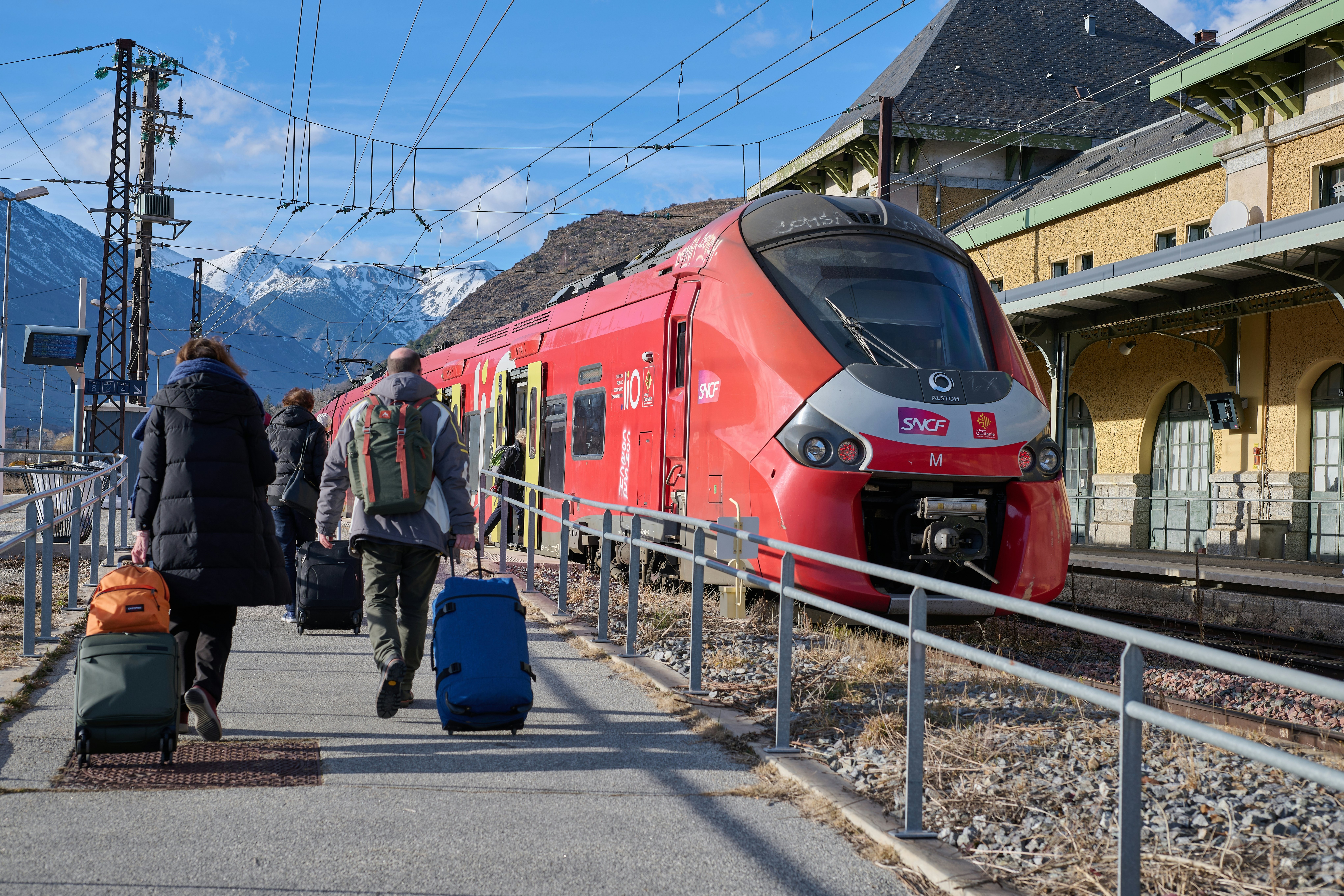 People board the train in Latour-de-Carol train station in France, with the mountains behind.