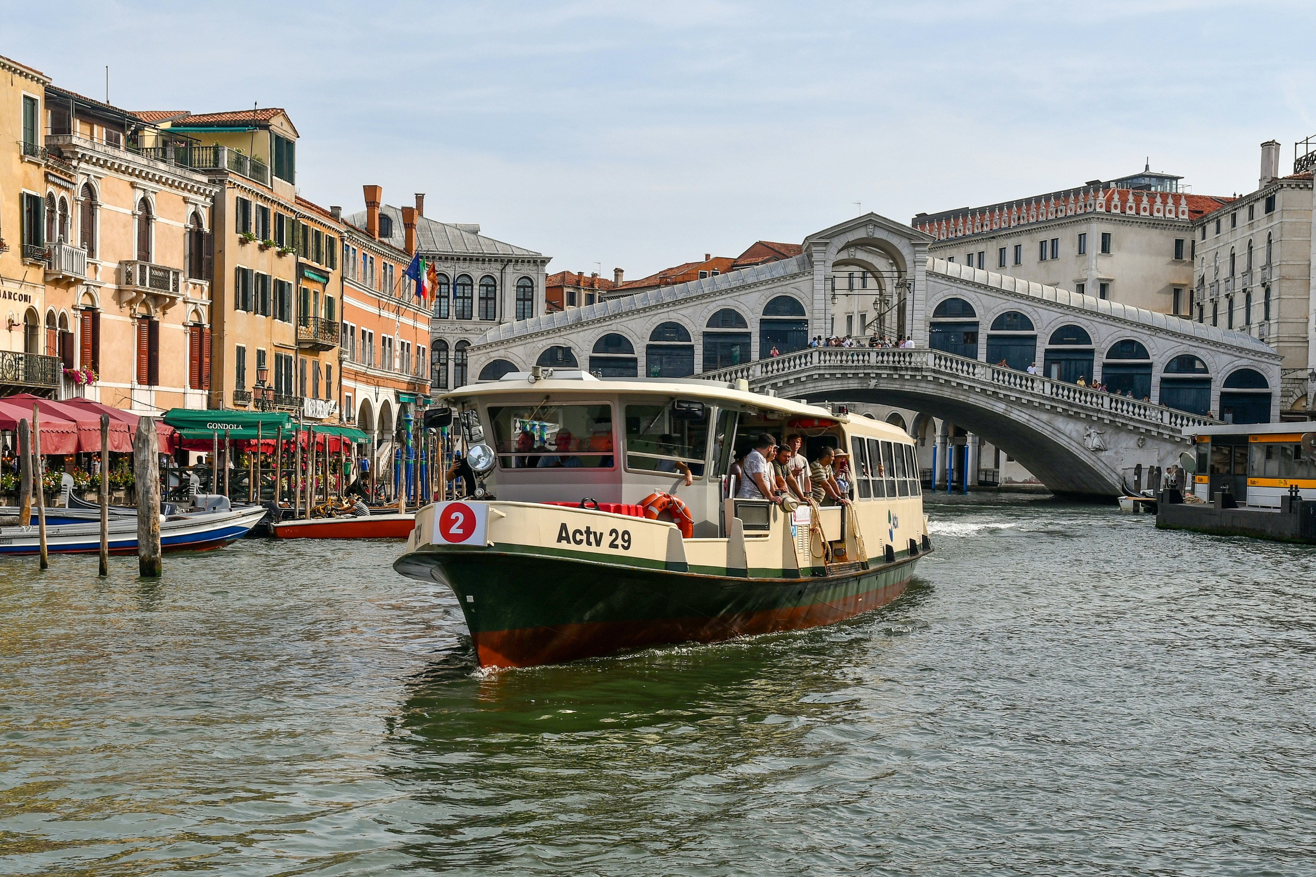 A passenger boat travels along a canal away from an ornate bridge.