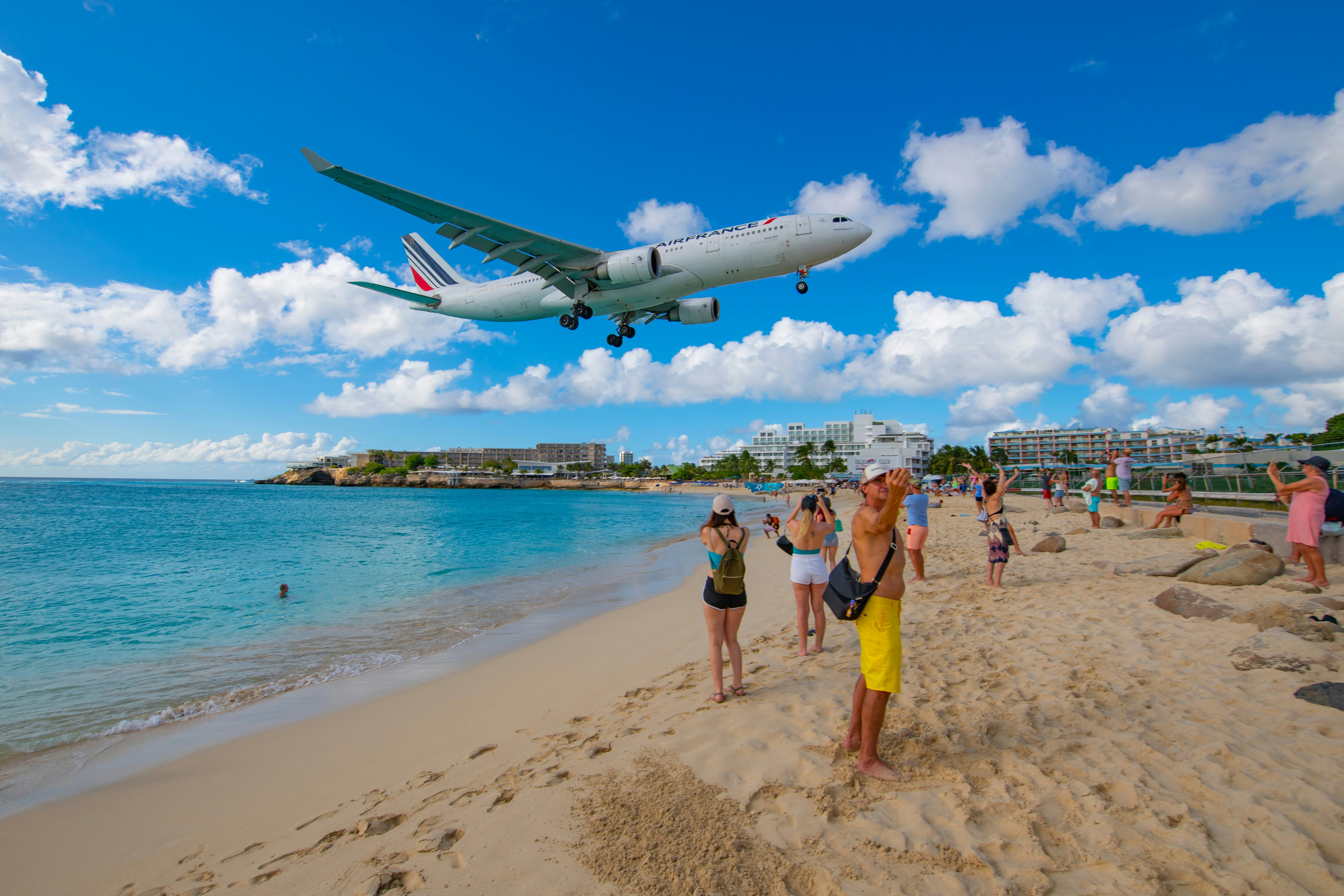 A jumbo jet flies low over a beach in a tropical island as it prepares to land.