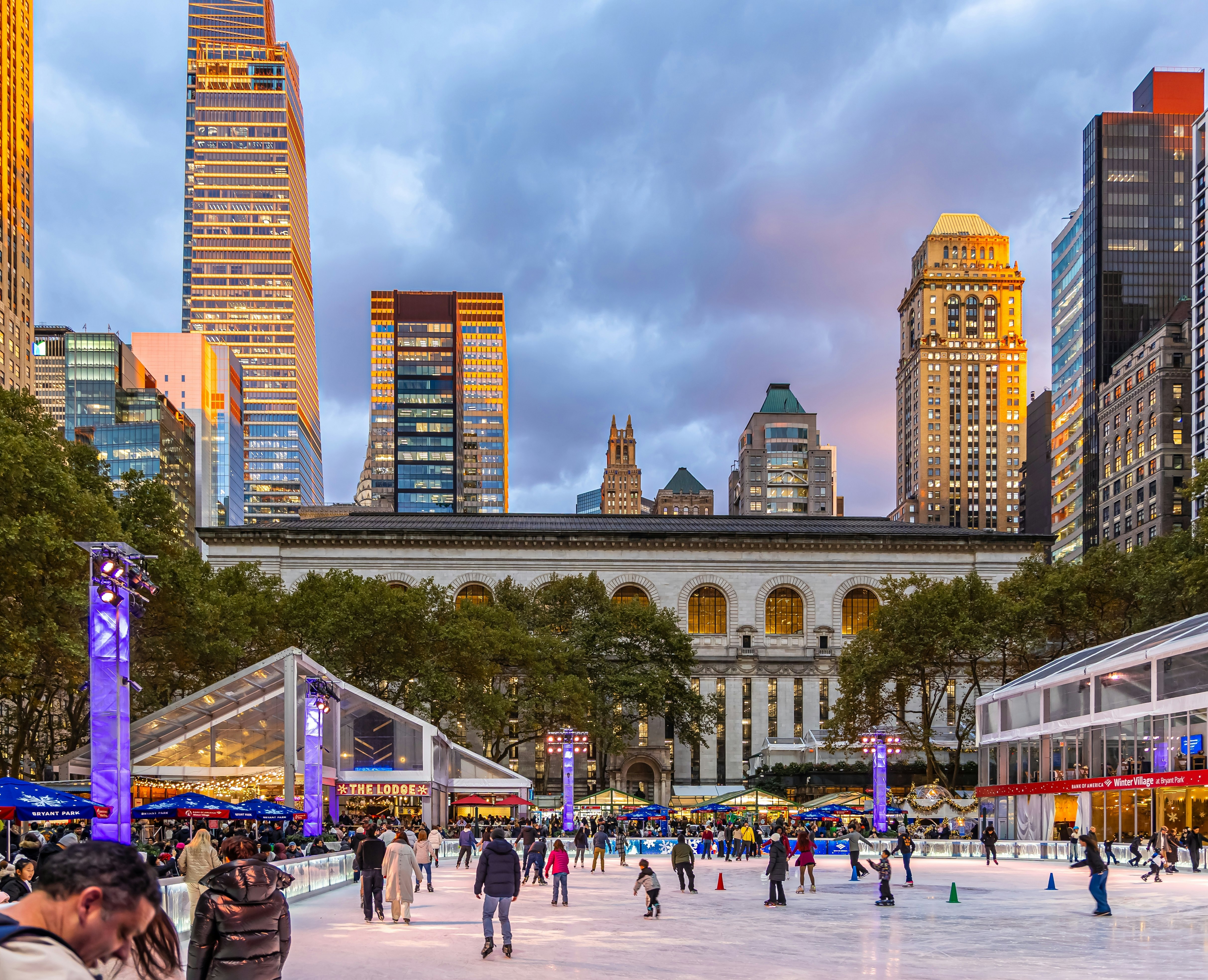 Winter holiday market and ice skating rink at Bryant Park with Midtown Manhattan skyline at sunset.