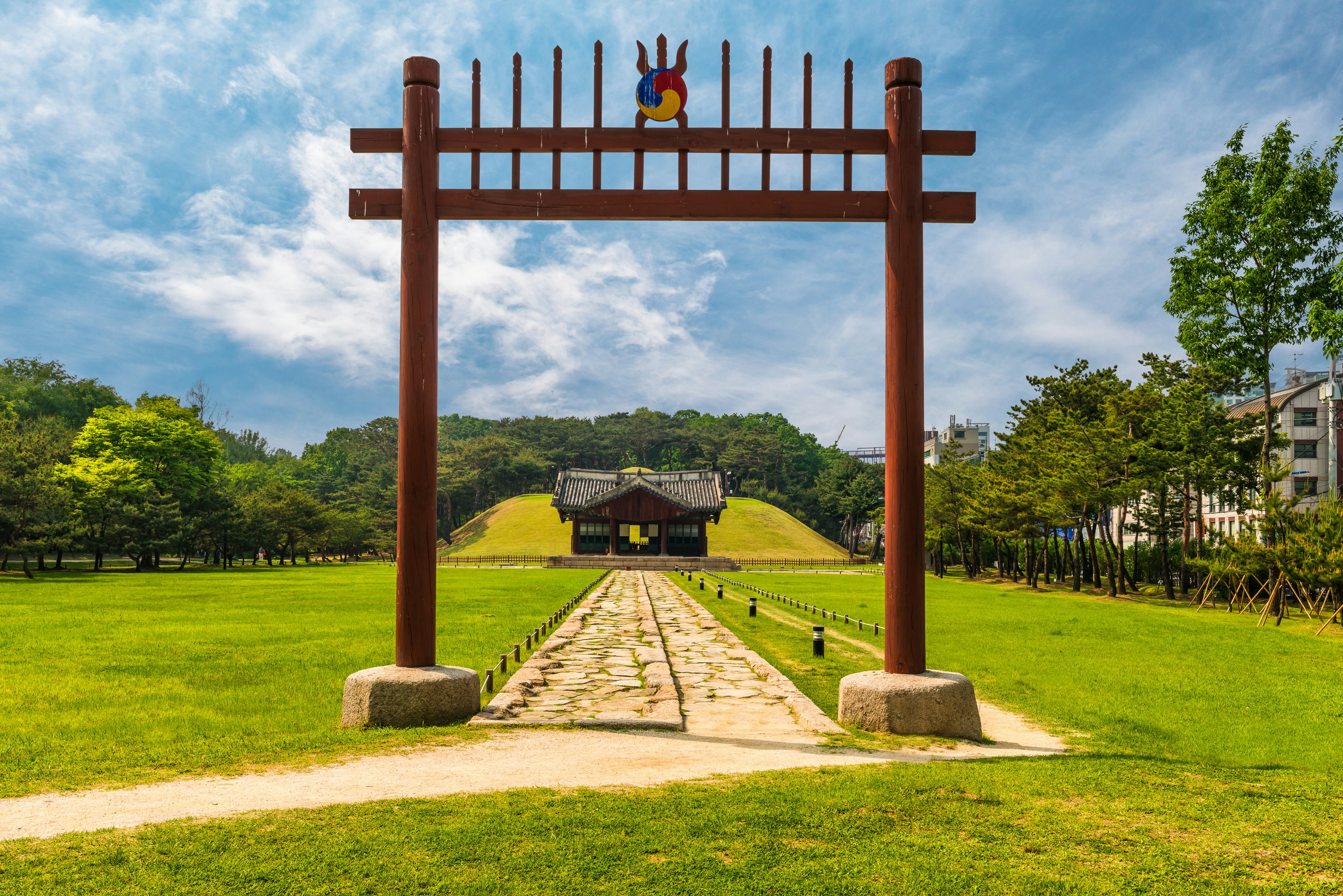 A gateway and pathway leading to a tomb in parkland.