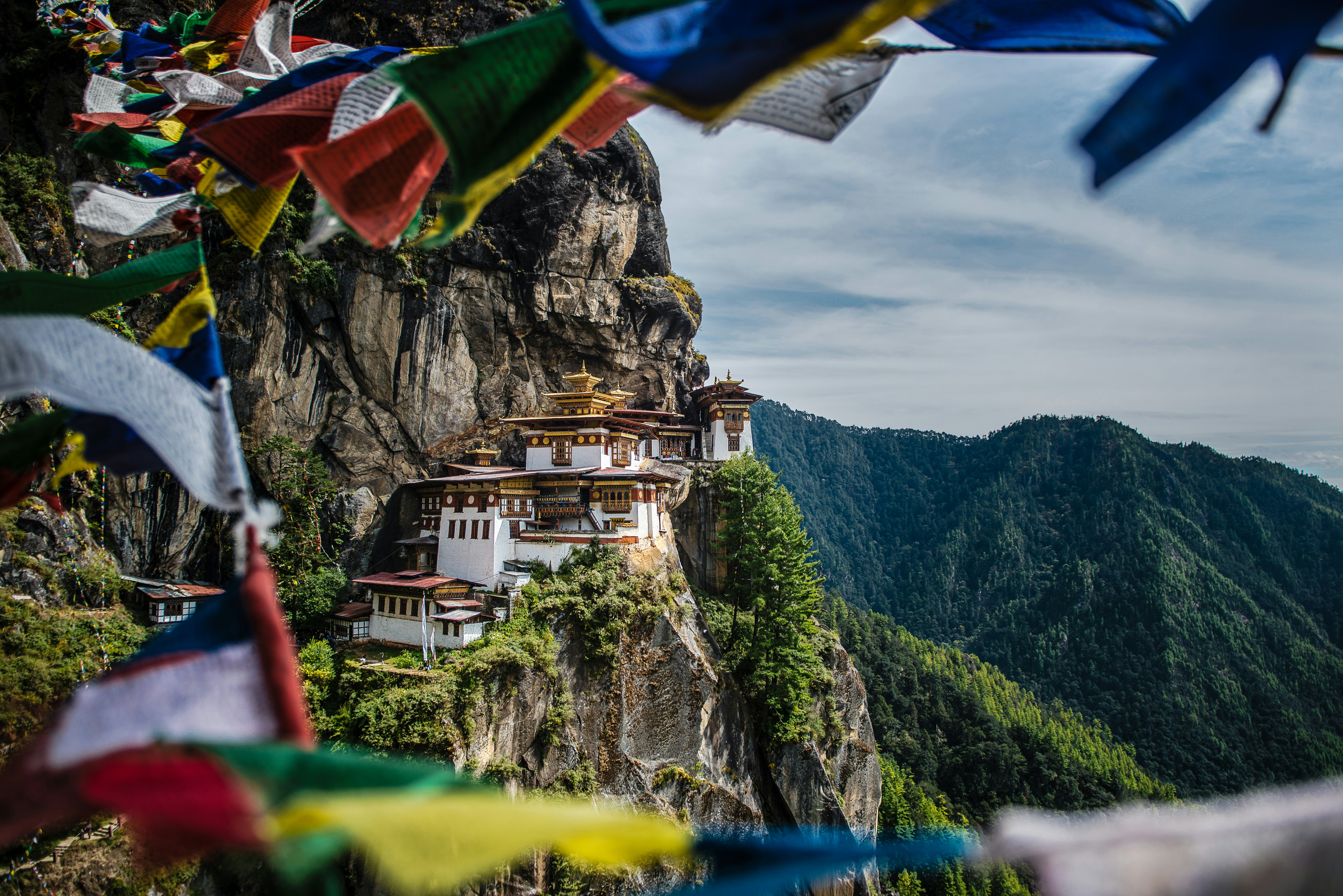 A white temple with colorful trim on a cliff's edge. Flags fly in the foreground
