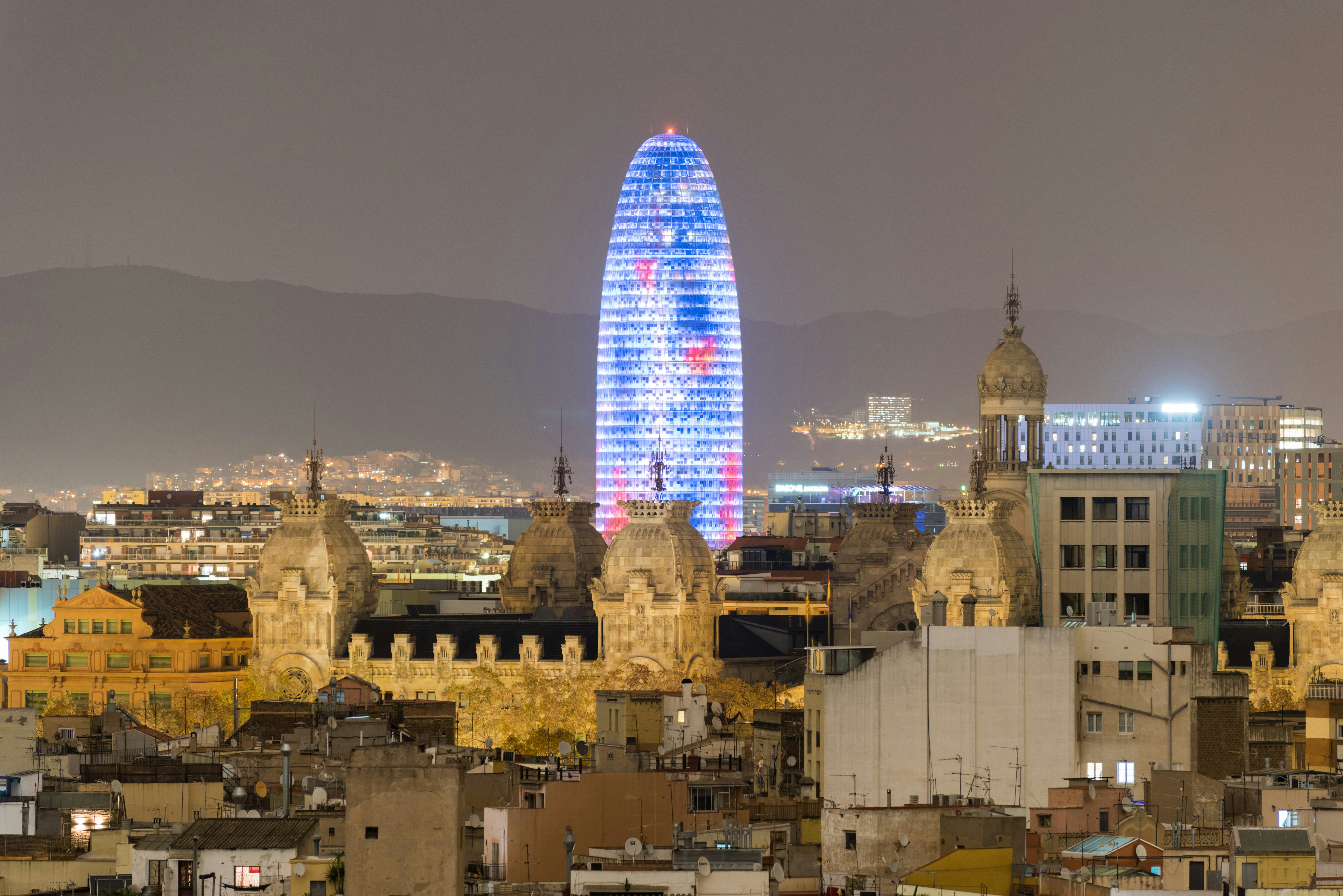 A glass tower in Barcelona, Spain, is lit up in blue and red at night.