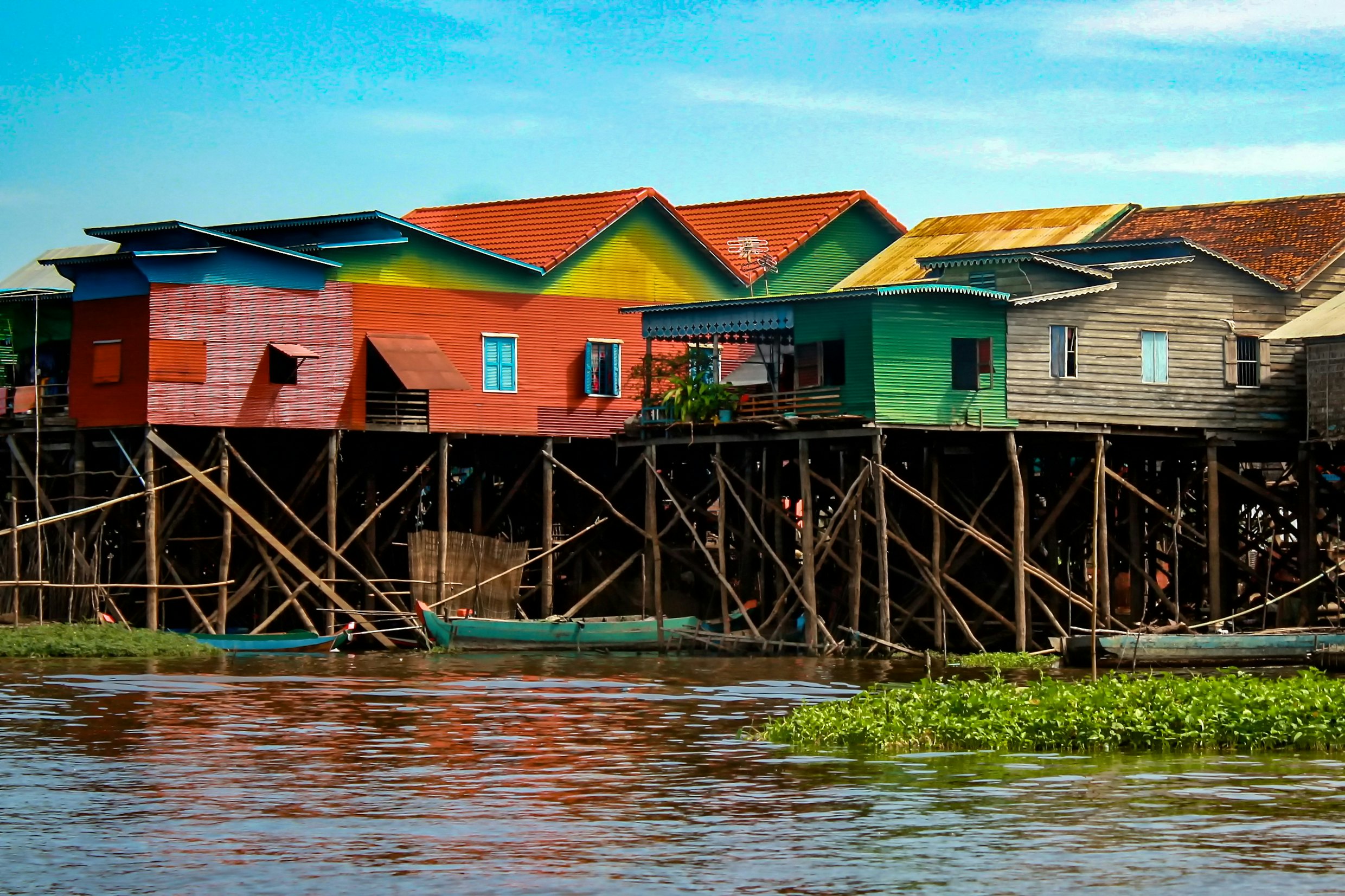 Colorful stilt houses standing above a river with small boats docked under them.